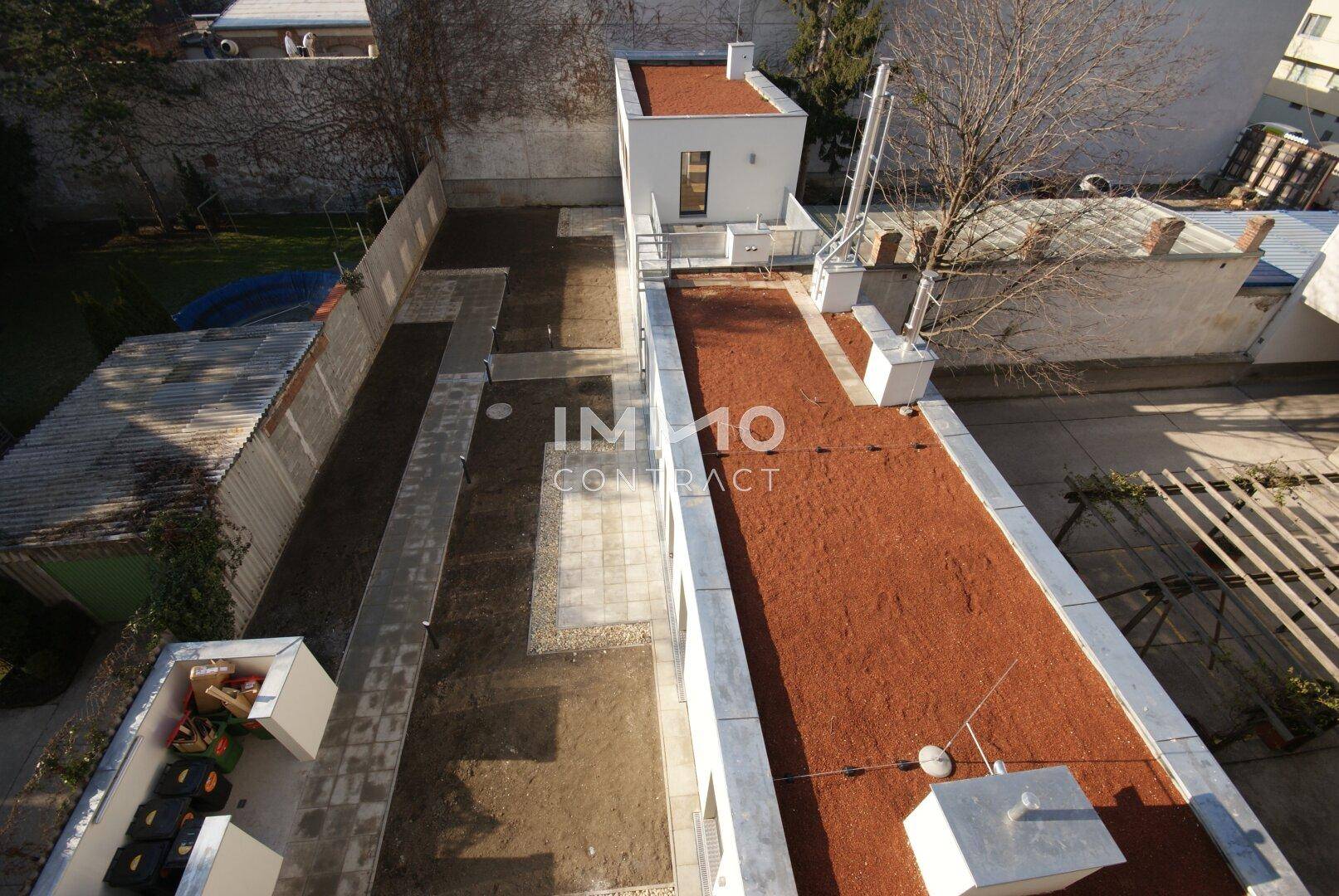 Luftaufnahme des Hinterhofs mit einem roten Flachdachgebäude und einem ungestalteten Gartenbereich.