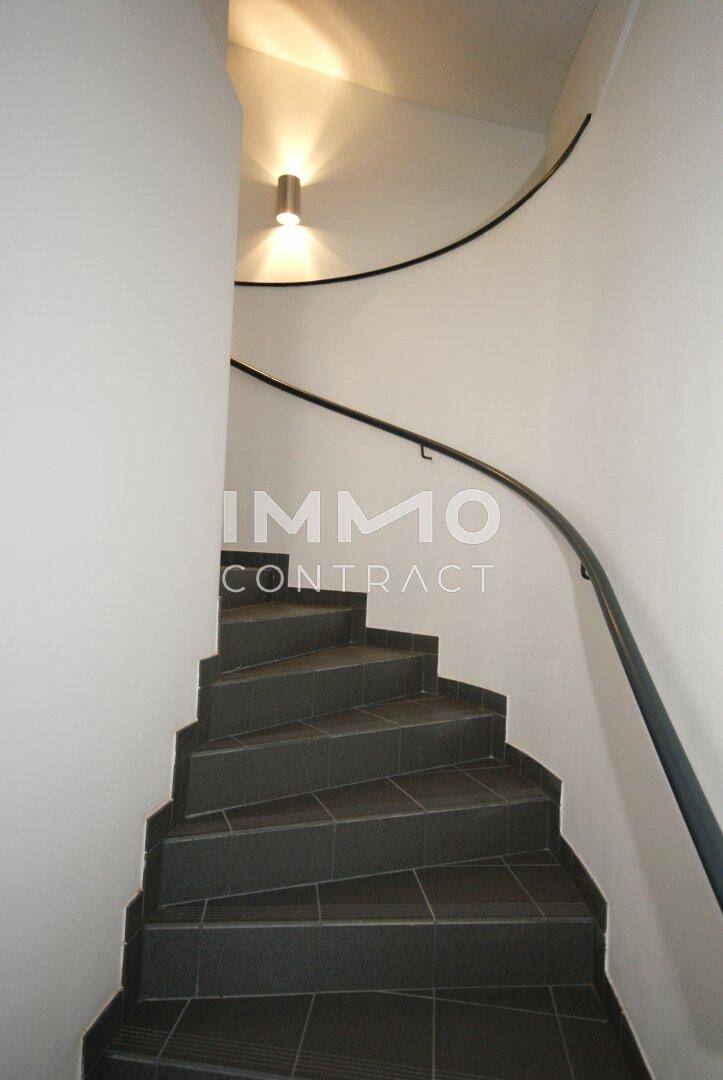 Moderne Wendeltreppe mit dunklen Fliesenstufen und einem schlichten Handlauf in einem hellen Treppenhaus.