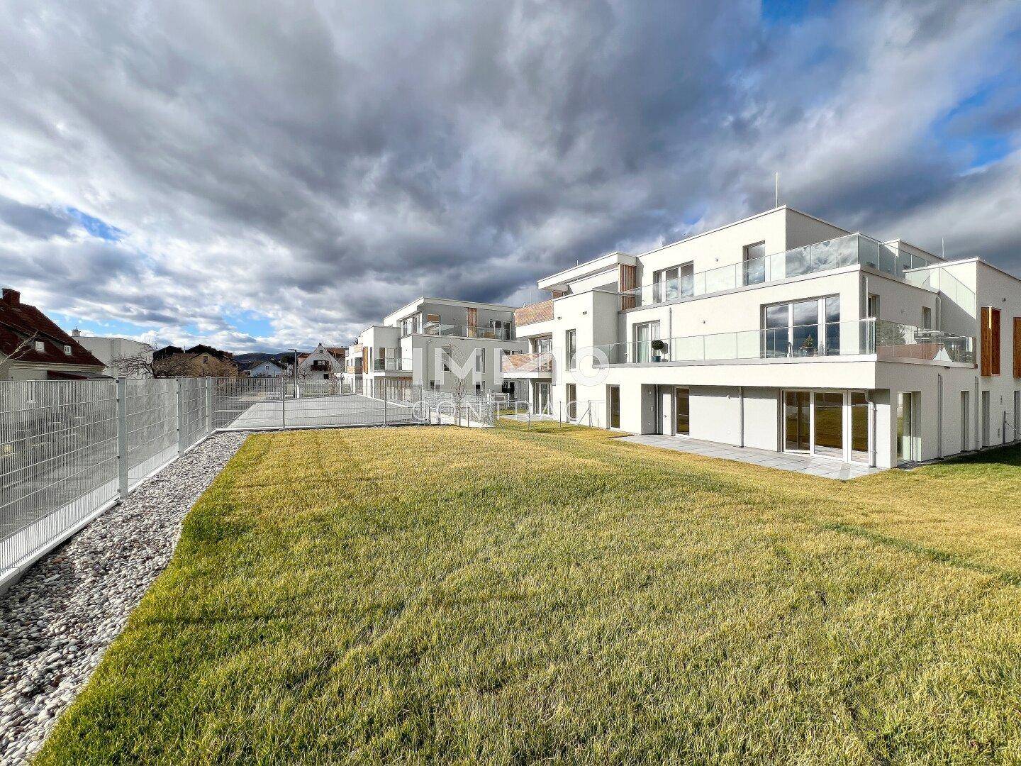 Moderne Wohnanlage mit mehreren Einheiten, großen Glasfronten und Balkonen, umgeben von einer grünen Rasenfläche.