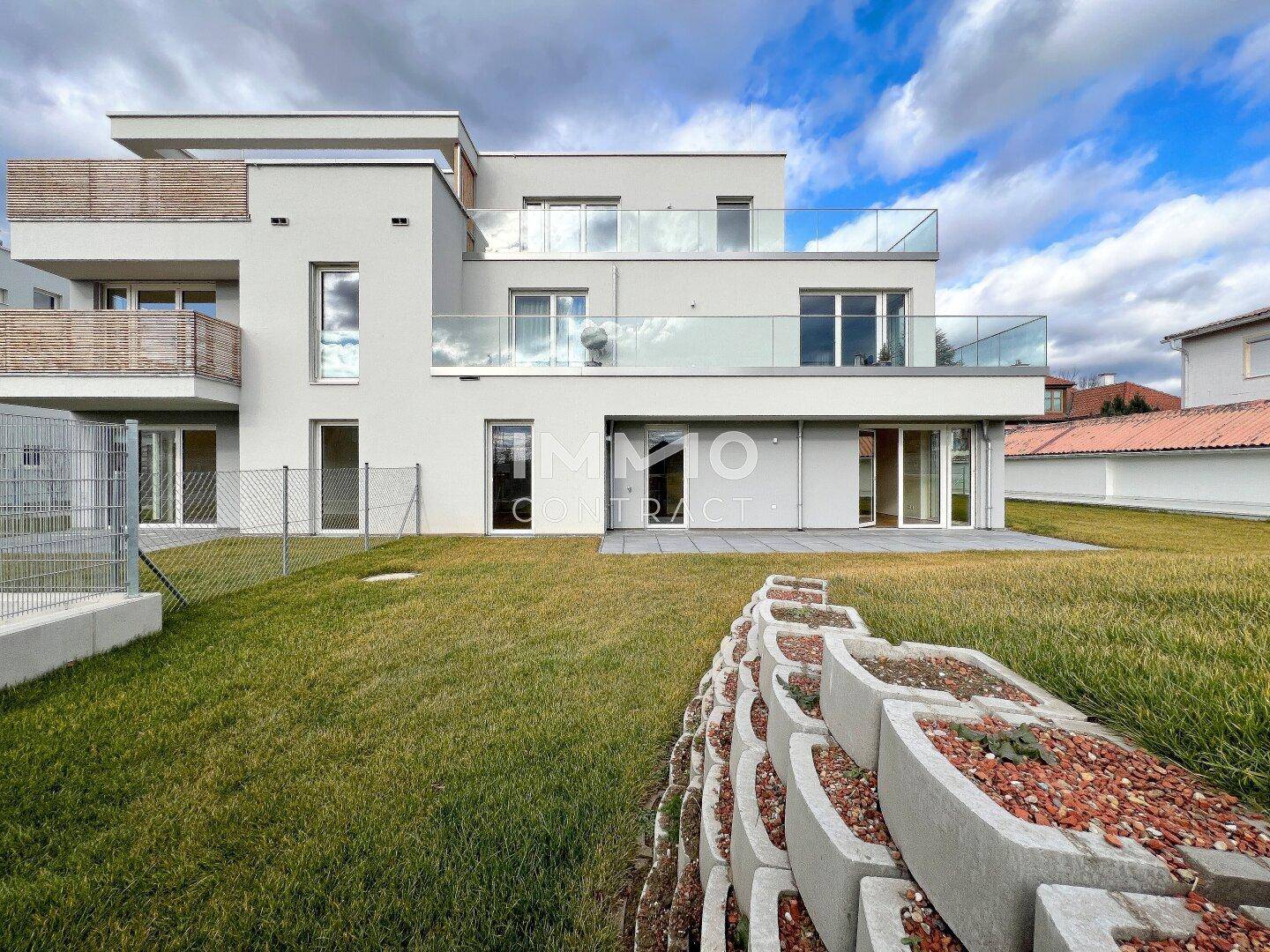 Ansicht der modernen Wohnanlage mit Terrassen, Balkonen und einer begrünten Böschung im Vordergrund.