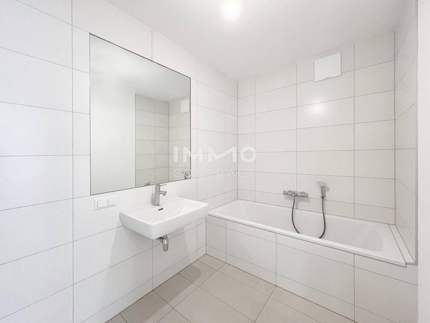 Modernes Badezimmer mit weißen Fliesen, einer Badewanne und einem einzelnen Waschbecken mit großem Spiegel.