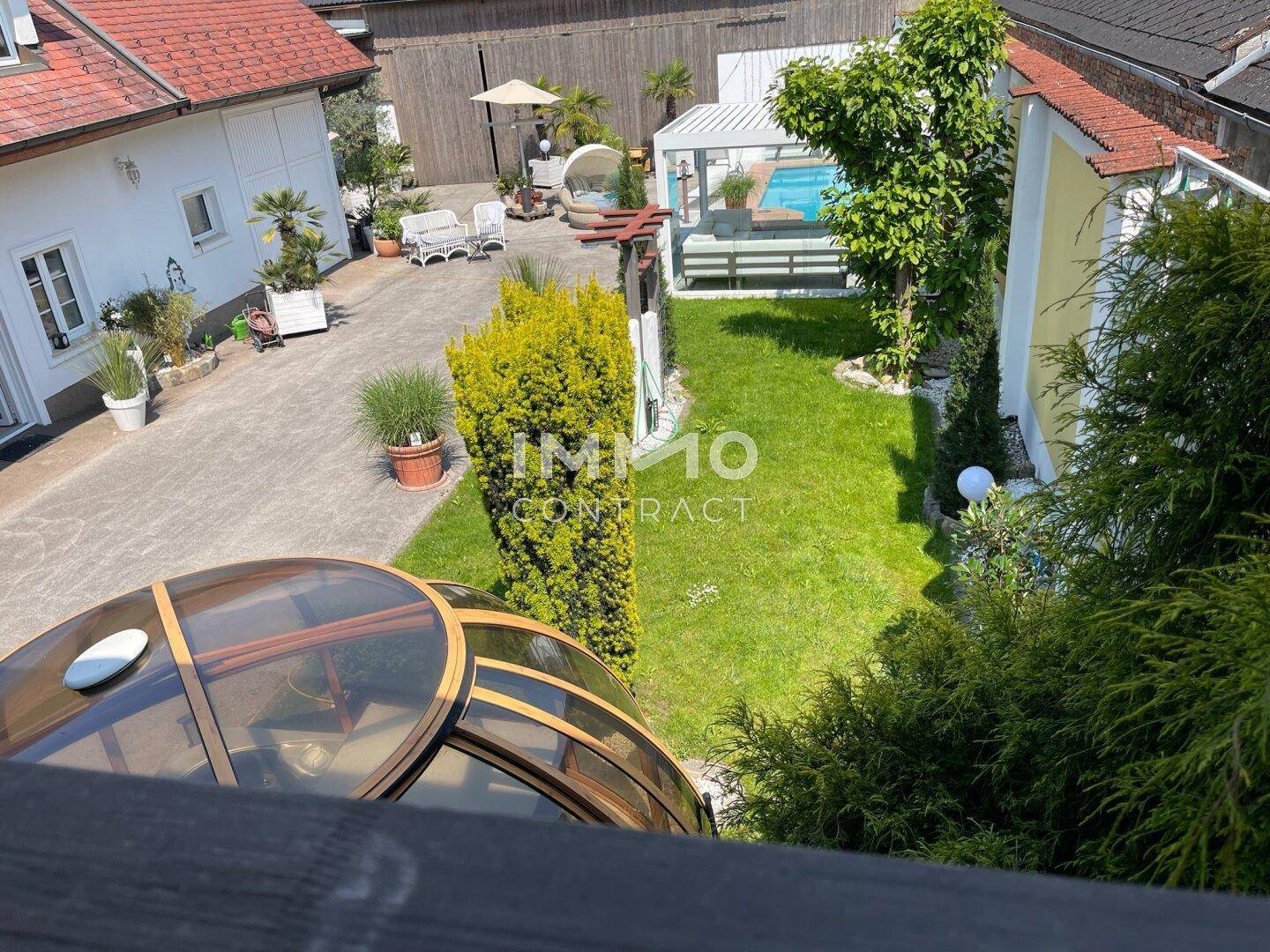 Vogelperspektive auf den weitläufigen Gartenbereich mit Rasenfläche, Pool und verschiedenen Gebäuden.