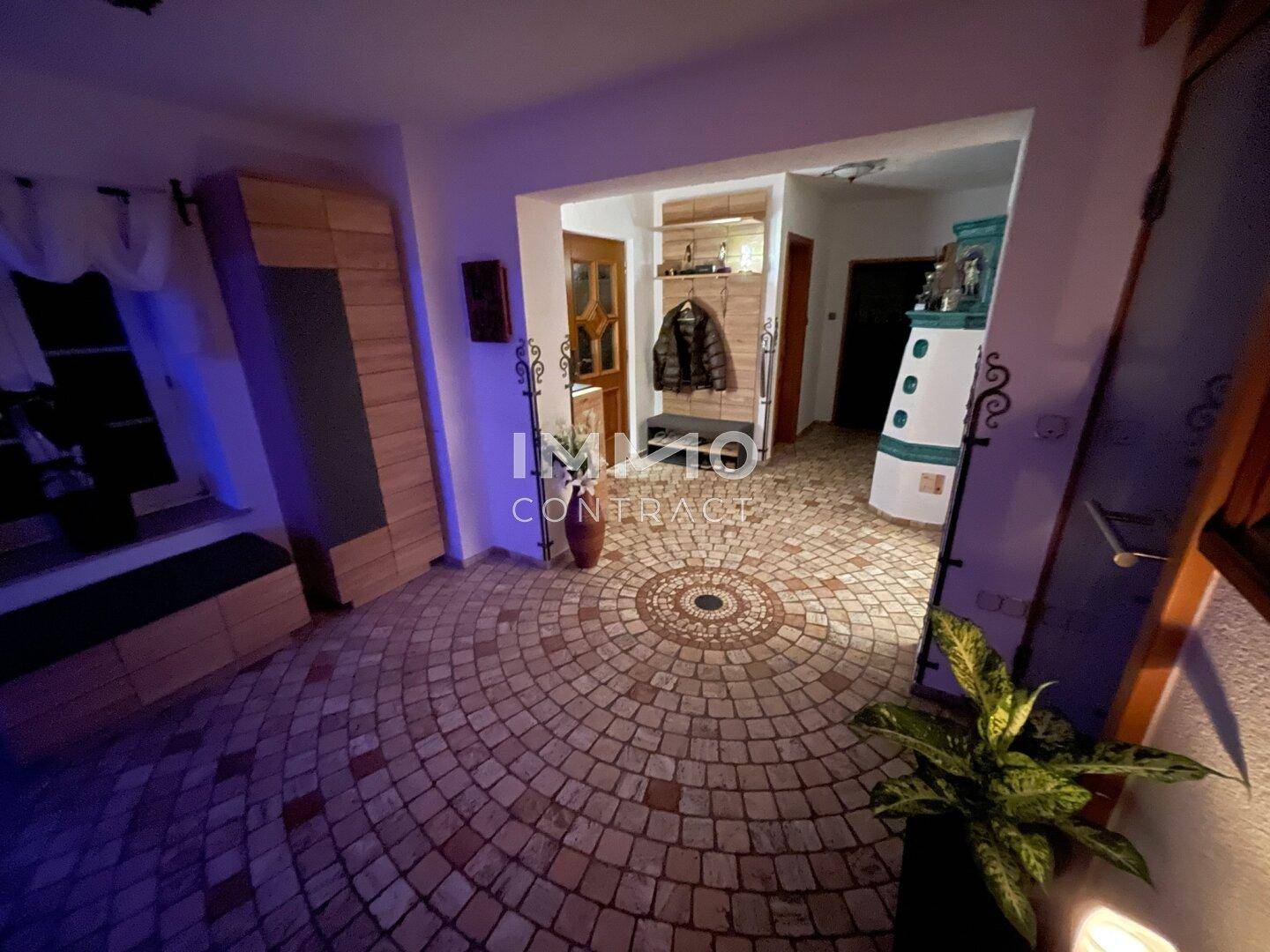 Einladender Eingangsbereich mit gemustertem Fliesenboden, Garderobe und traditionellem Kachelofen.
