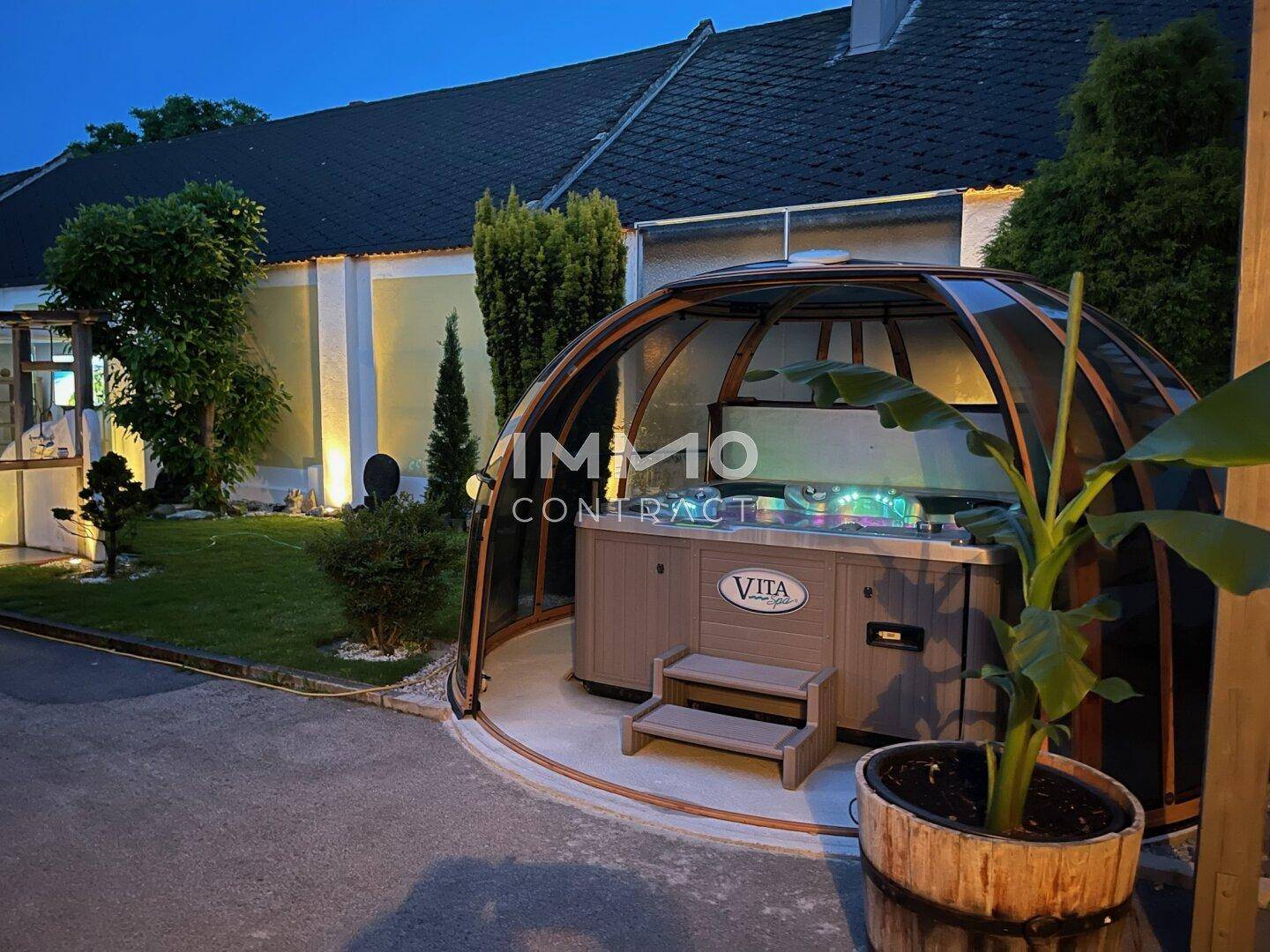 Whirlpool in einem modernen Glaskuppel-Pavillon im gepflegten Gartenbereich.