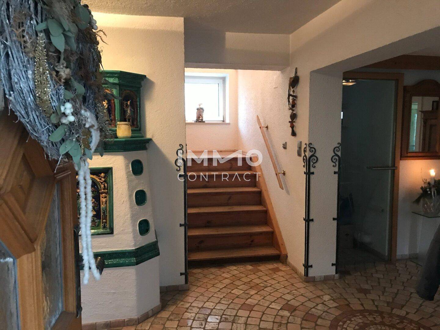 Geräumiger Eingangsbereich mit gemustertem Fliesenboden, Holztreppe und traditionellem Kachelofen.