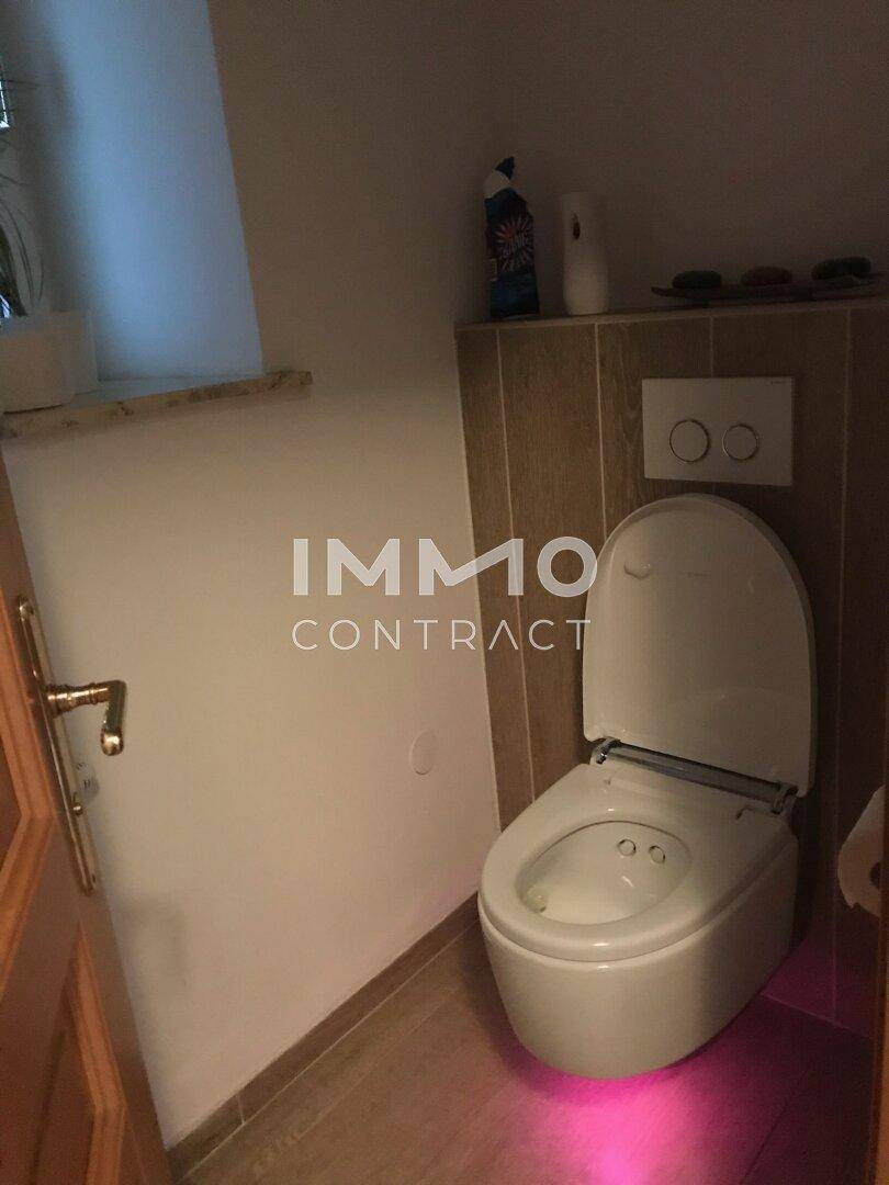 Modernes WC mit Fenster, Fliesenboden und indirekter Beleuchtung unter der Toilette.