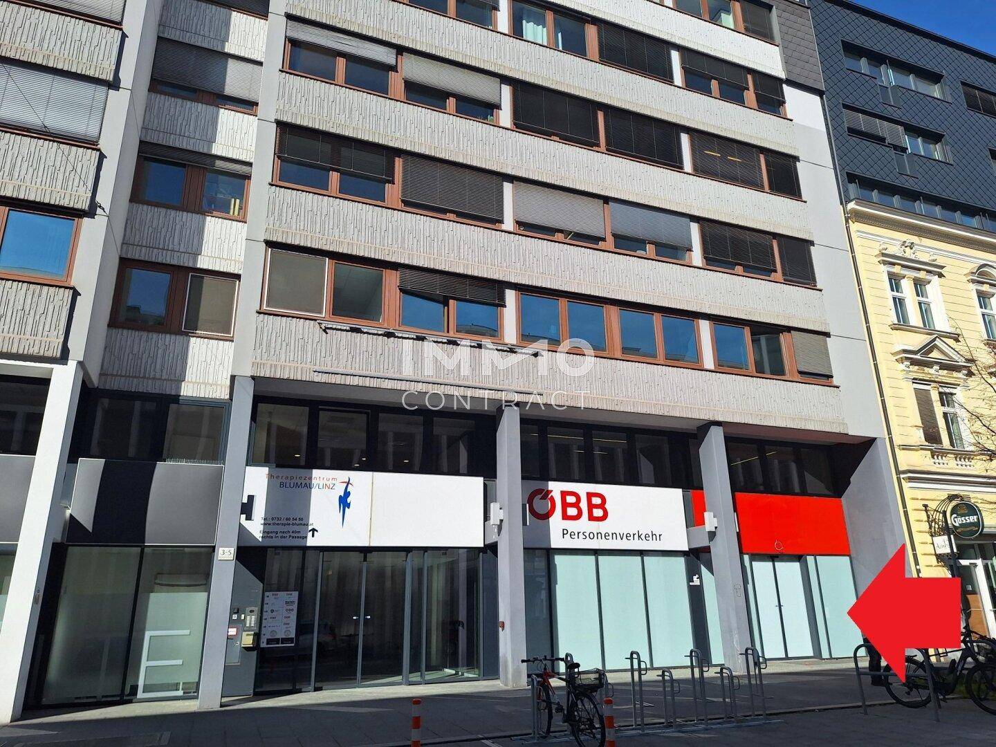 Moderne Geschäftsfassade mit großen Fenstern und Eingängen, darunter eine Bankfiliale und andere Geschäfte.