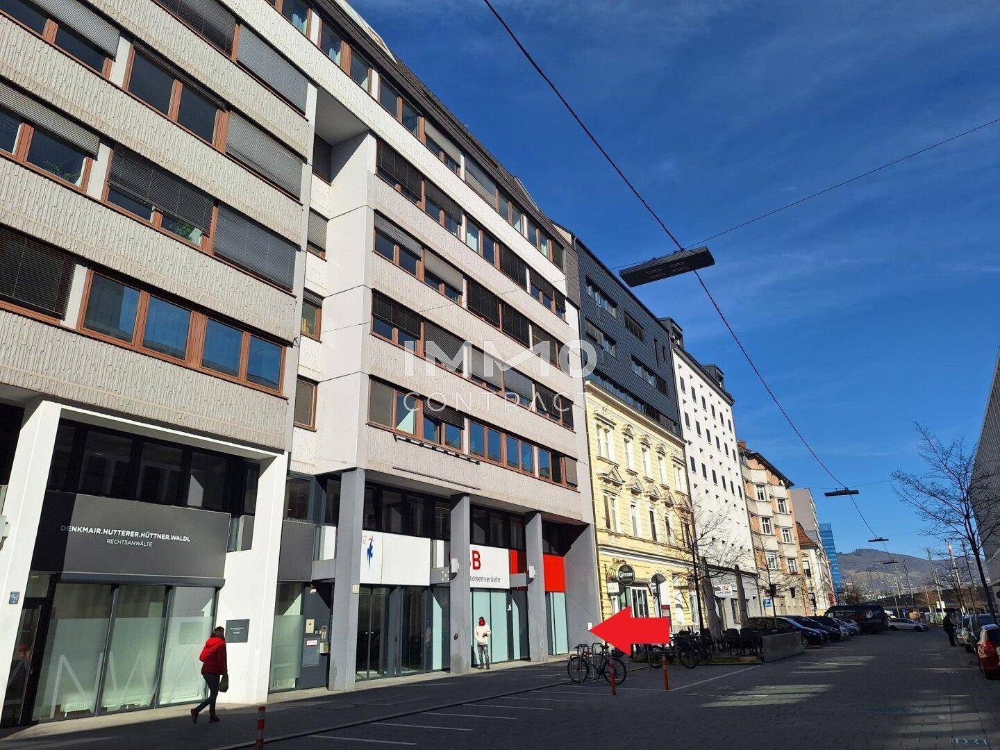 Mehrere Geschäftsgebäude entlang einer belebten Stadtstraße mit geparkten Fahrrädern und klarem blauem Himmel.