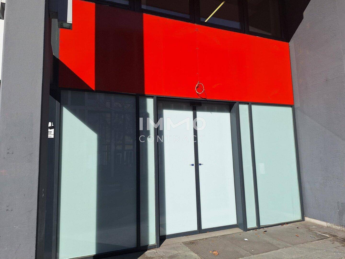 Moderne Geschäftsfassade mit großen Schaufenstern und auffälliger roter Verkleidung über dem Eingangsbereich.