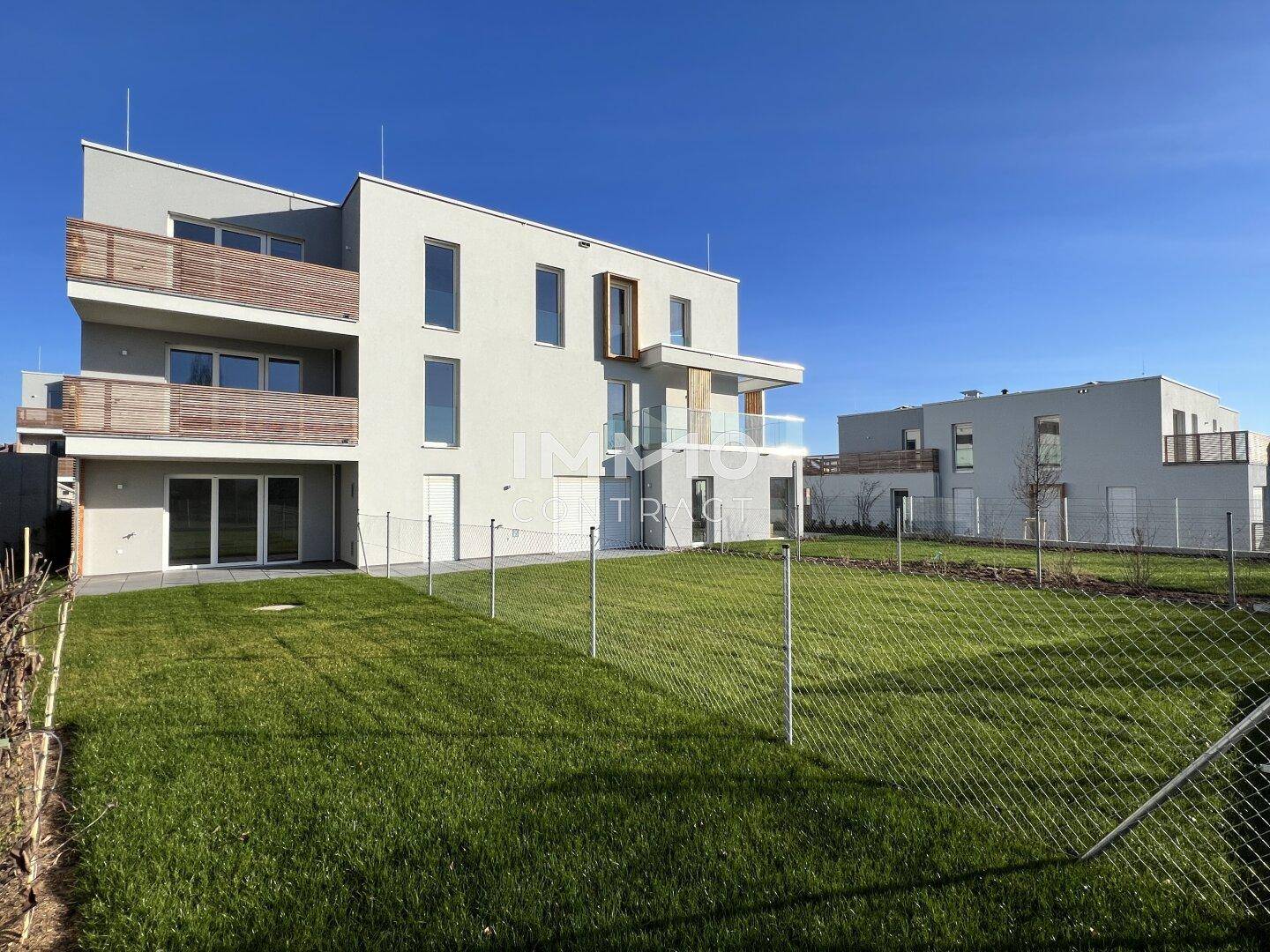 Neubauwohnungen mit modernen Fassaden, Balkonen und gepflegten Rasenflächen unter strahlend blauem Himmel.
