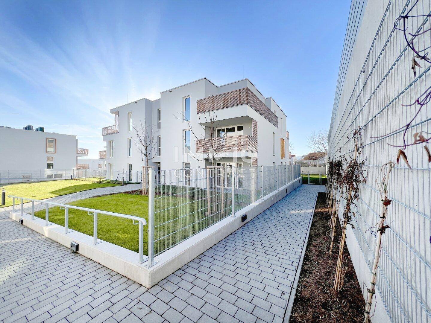 Neubau-Wohngebäude mit moderner Architektur, umzäunten Grünflächen und gepflastertem Weg.
