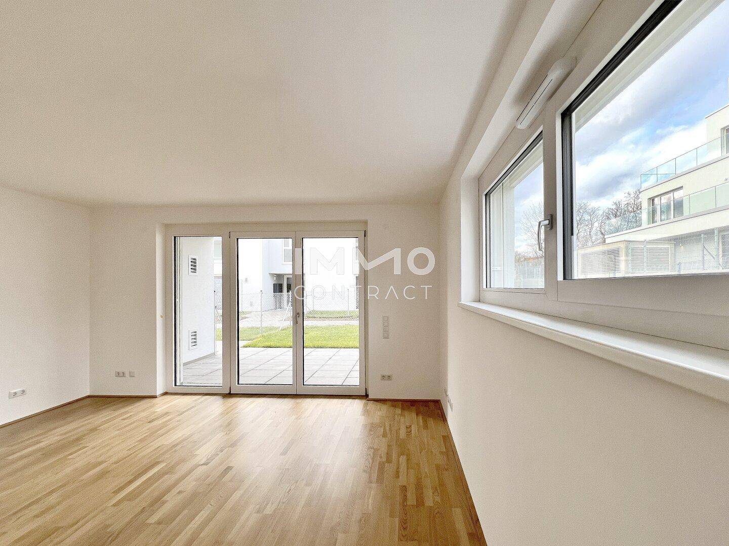 Geräumiges Wohnzimmer mit Holzboden, großen Fenstern und Zugang zur Terrasse.