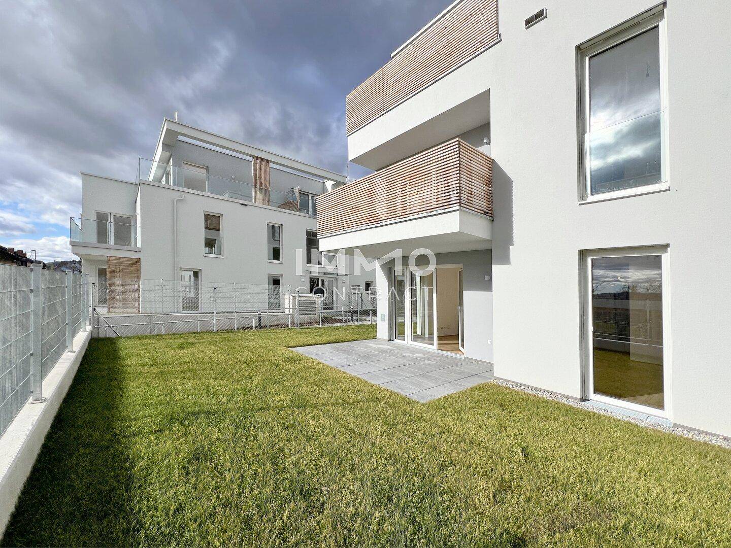 Außenansicht eines Neubaus mit Terrasse, Rasenfläche und modernen Balkonen.