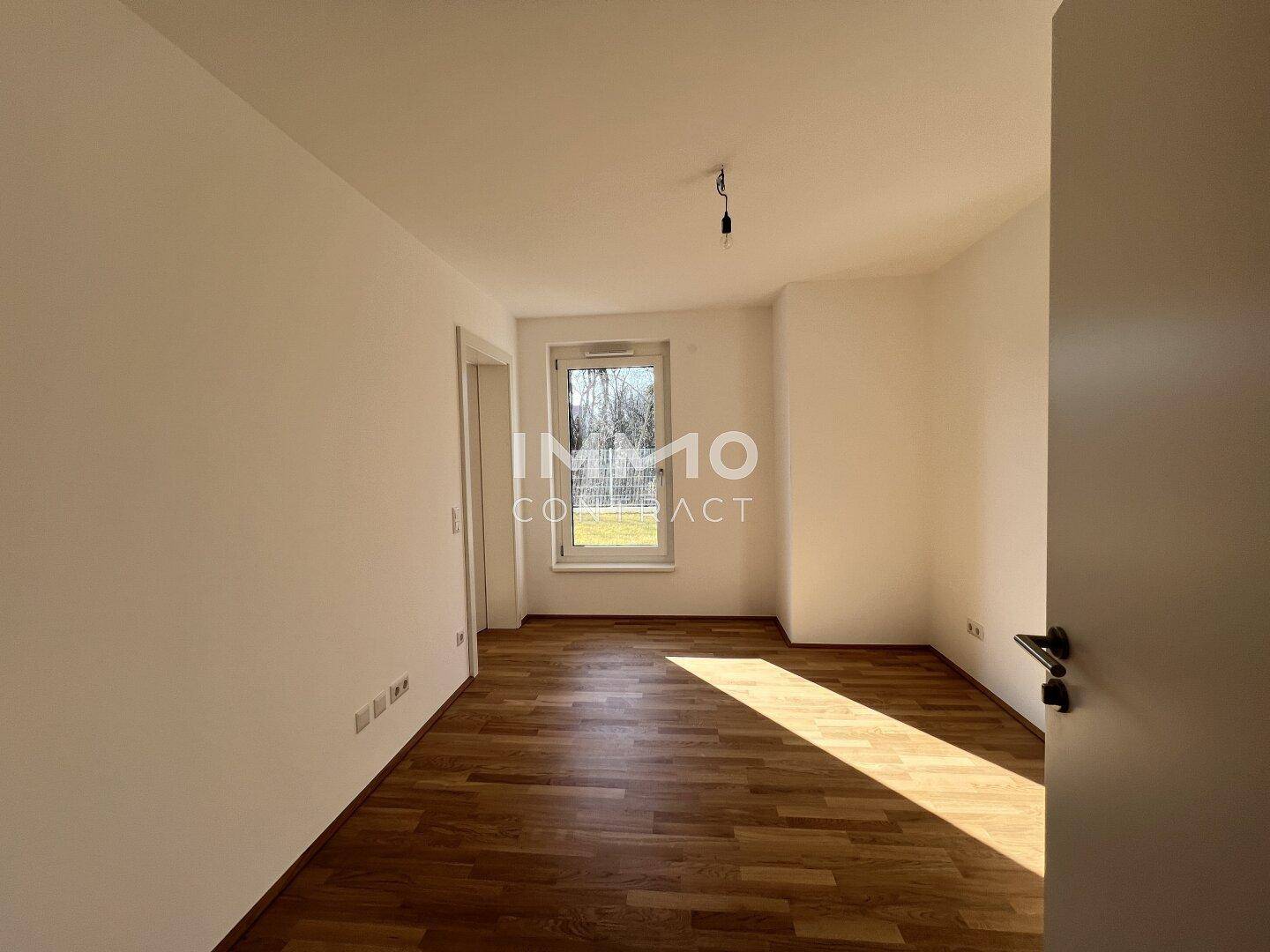 Gemütliches Schlafzimmer mit hellem Parkettboden und einem Fenster mit Blick ins Grüne.