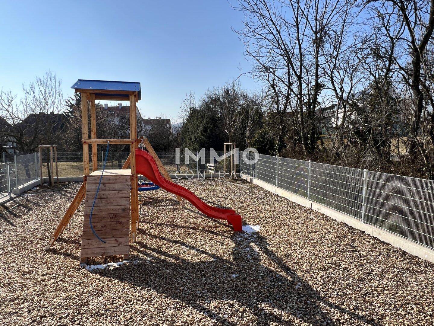 Nahaufnahme eines Spielplatzes mit Rutsche und Kletterturm, umzäunt für Sicherheit.
