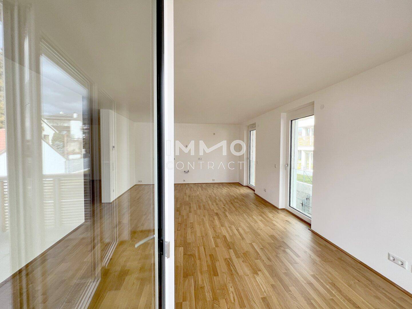 Geräumiges, leeres Wohnzimmer mit großen Fenstern und hellem Parkettboden.