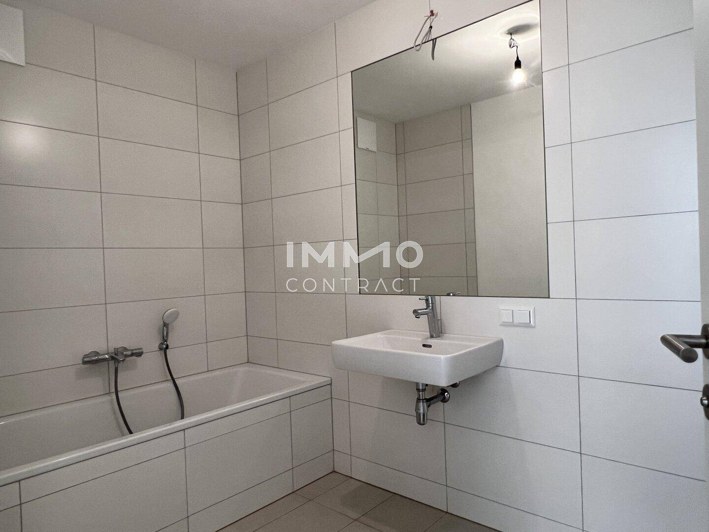 Modernes Badezimmer mit Badewanne, weißen Fliesen und einem großen Wandspiegel.