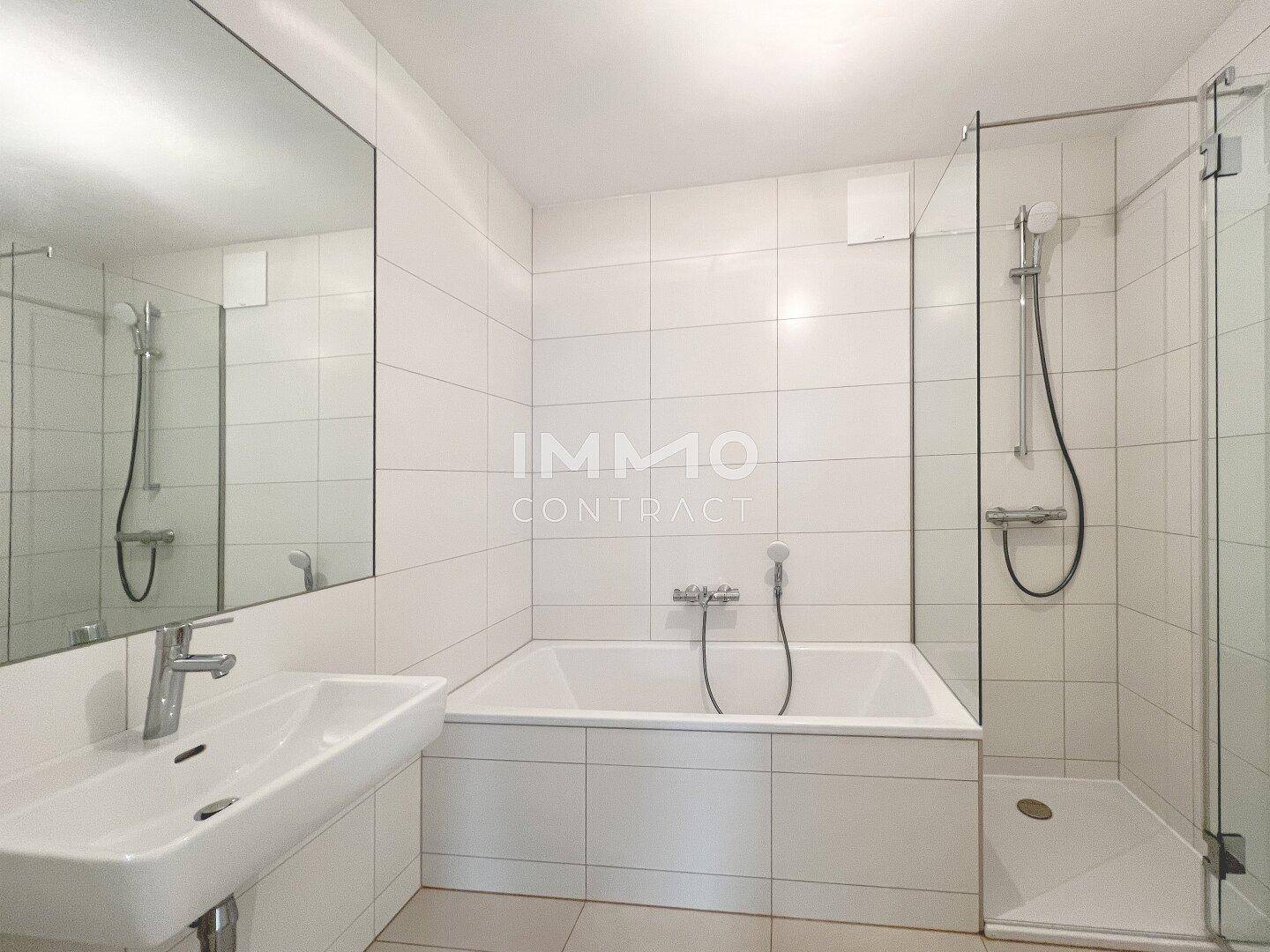 Modernes Badezimmer mit Badewanne, Dusche und weißen Fliesen.