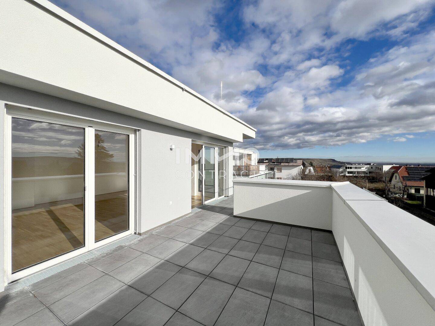Geräumige Terrasse mit Fliesenboden und weitem Blick über die Umgebung unter bewölktem Himmel.