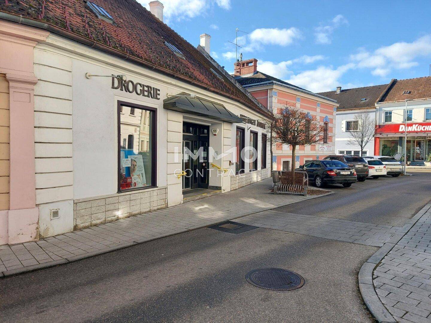 Straßenansicht einer Drogerie in einem historischen Gebäude mit weiteren Geschäften im Hintergrund.