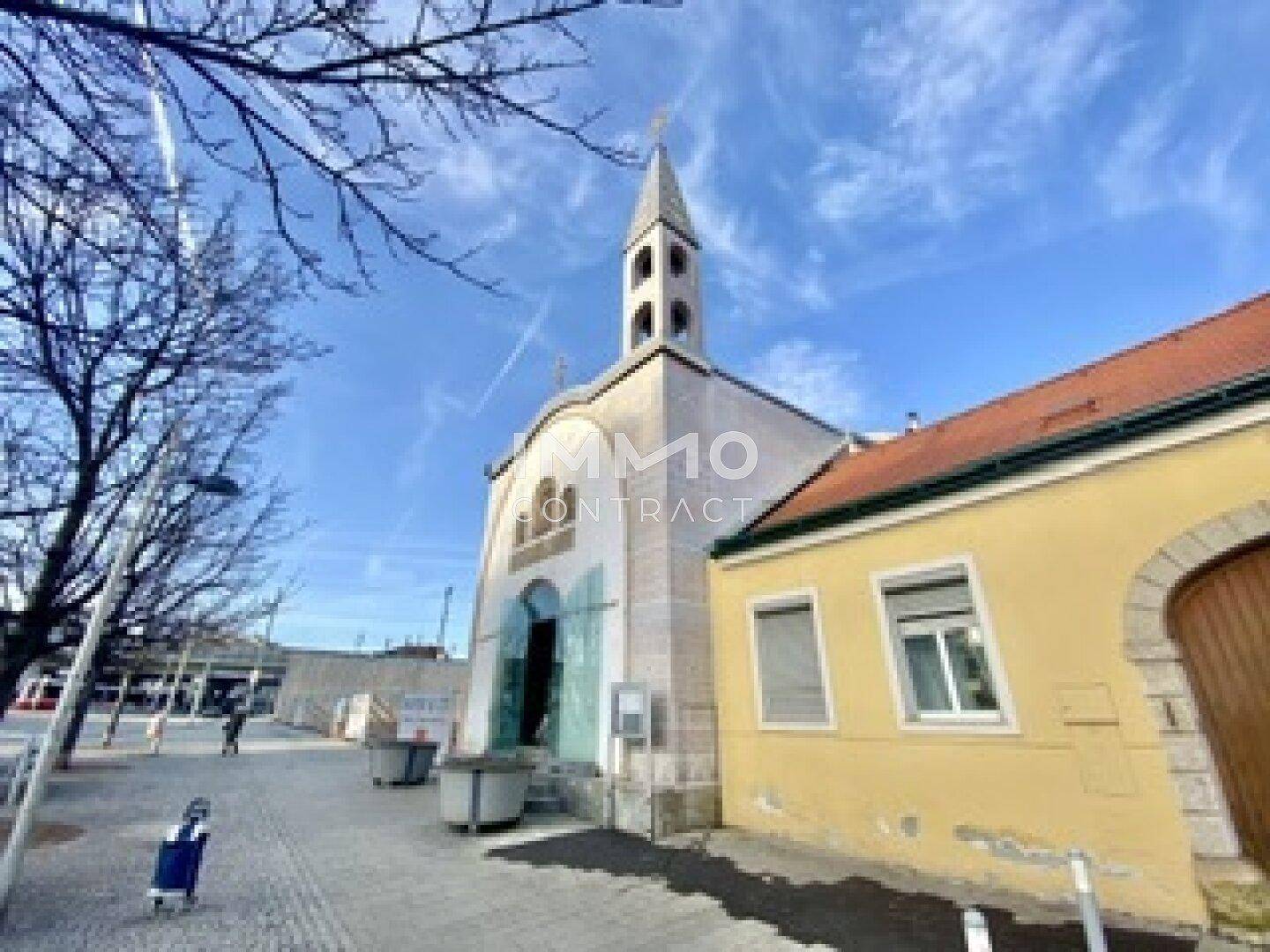 Historische Kirche mit Turm und angrenzendem Gebäude an einer Straße.
