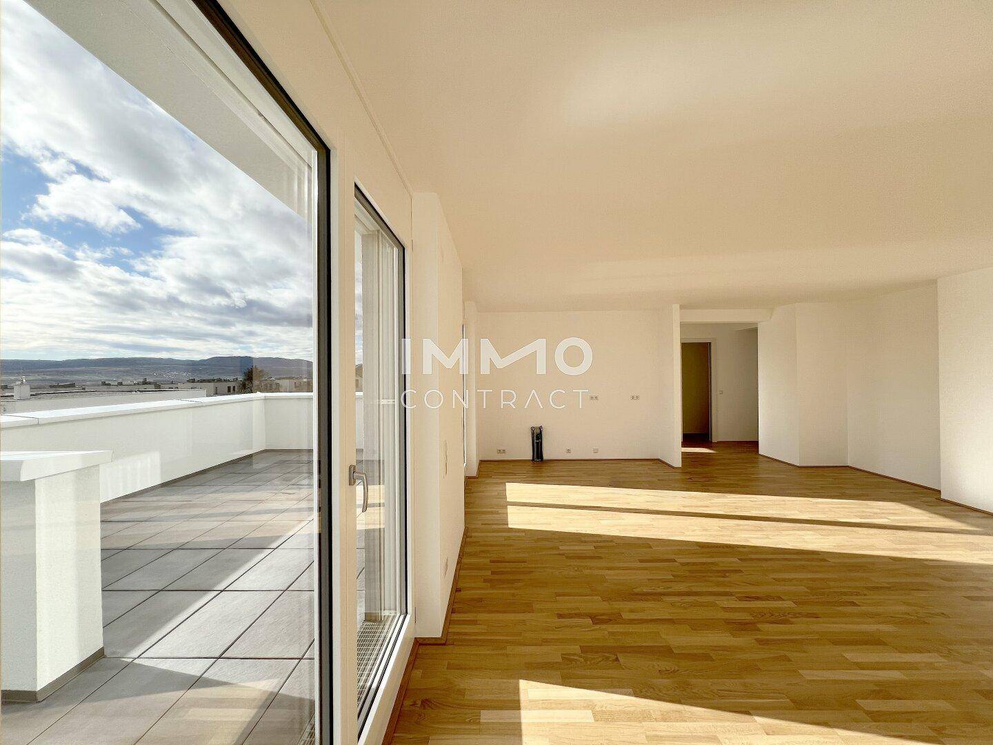 Geräumiger, leerer Wohnbereich mit hellem Parkettboden und großen Fenstern zur Terrasse.