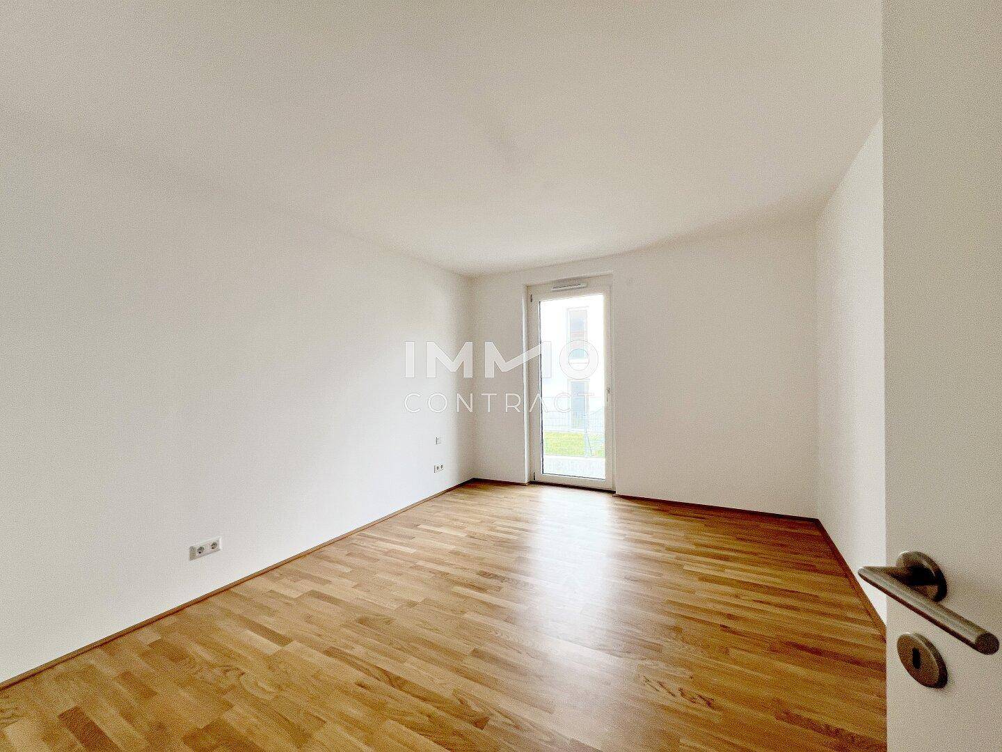 Helles Zimmer mit Parkettboden und Zugang zu einem Außenbereich, ideal als Schlafzimmer.