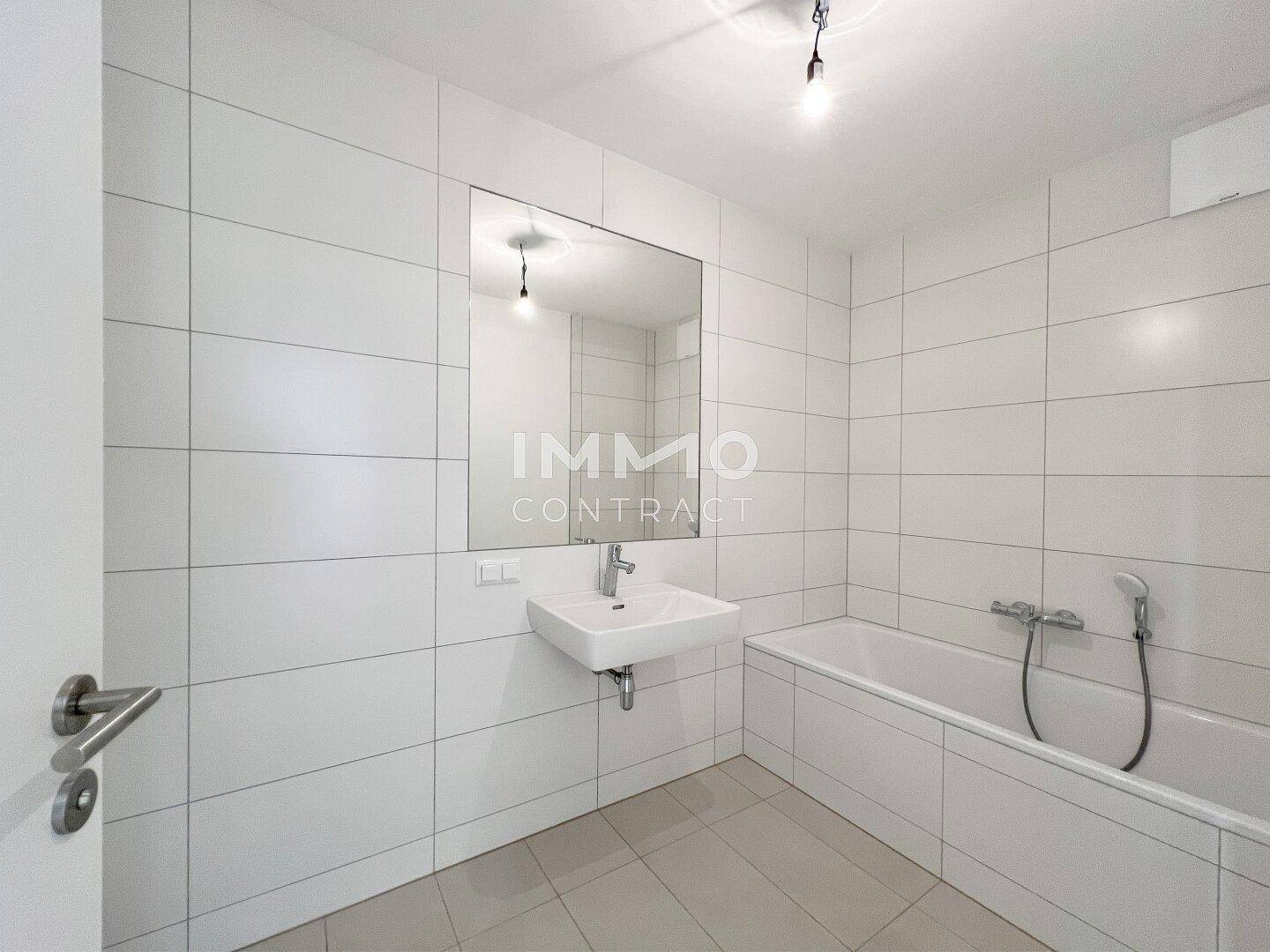 Modernes Badezimmer mit weißen Fliesen, Badewanne und Waschbecken in minimalistischem Design.