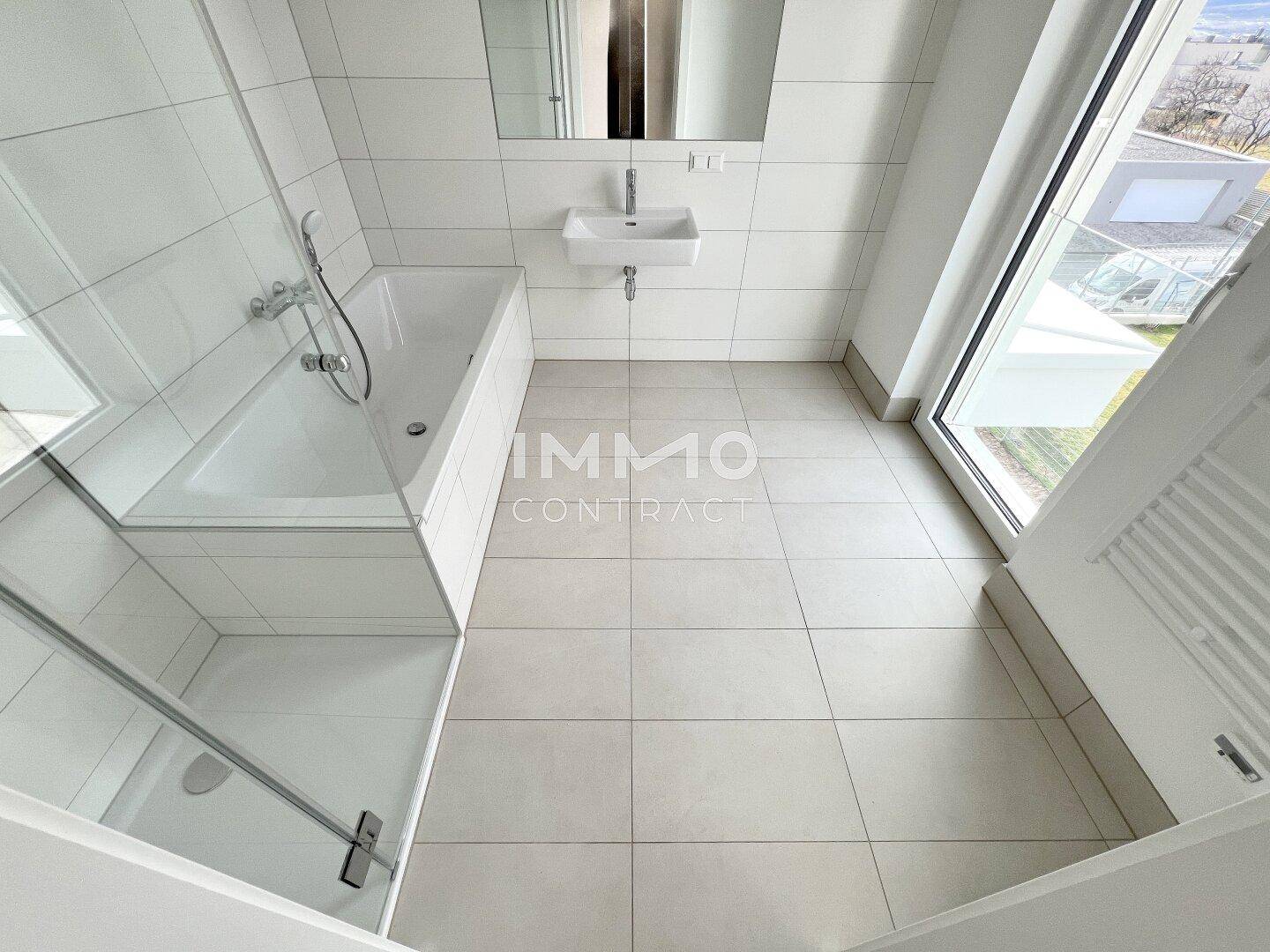 Helles Badezimmer mit Badewanne und Duschbereich, ausgestattet mit modernen Fliesen und Fenster.