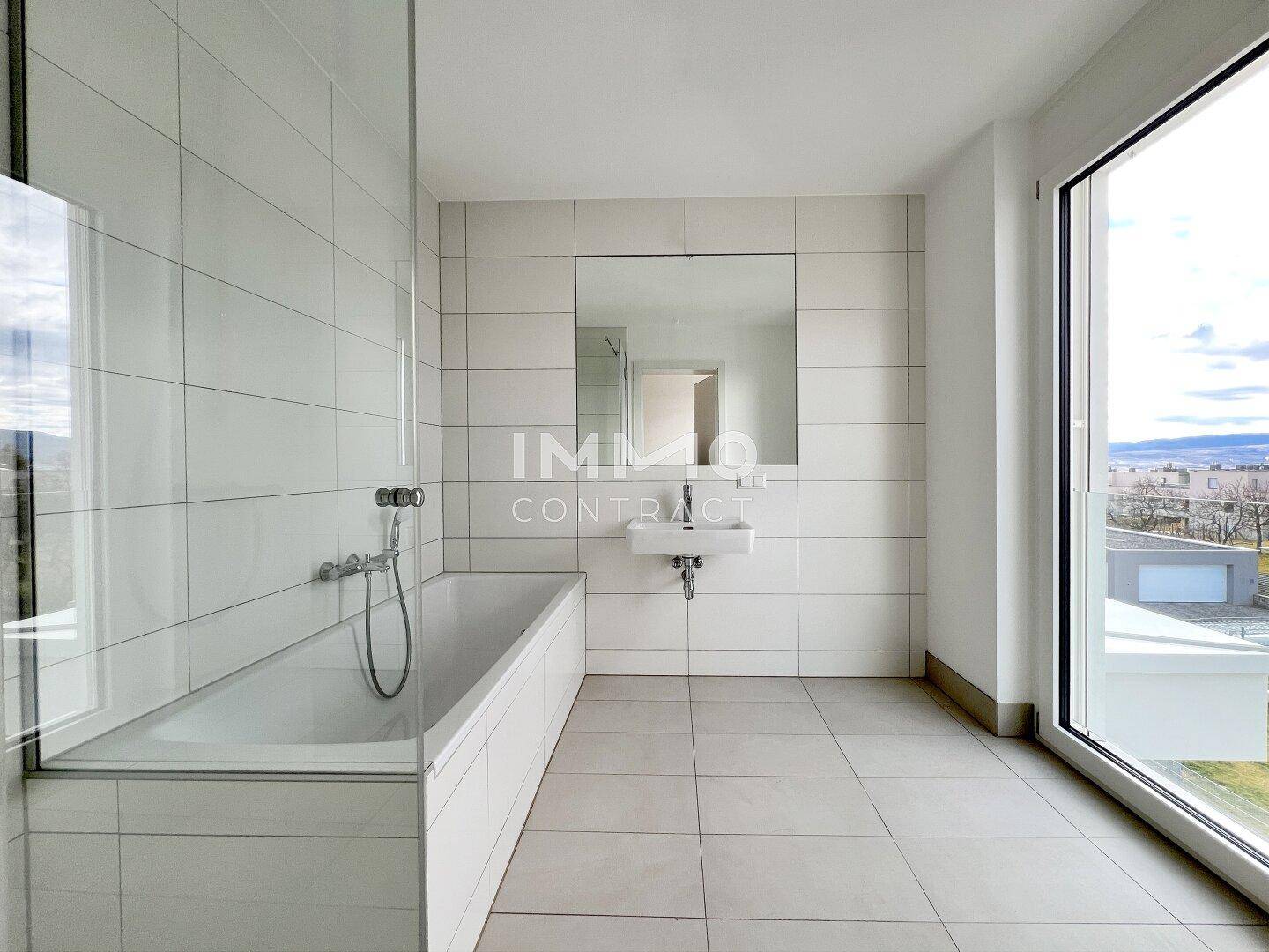 Modernes Badezimmer mit Badewanne, Fliesenboden und großem Fenster für viel Tageslicht.