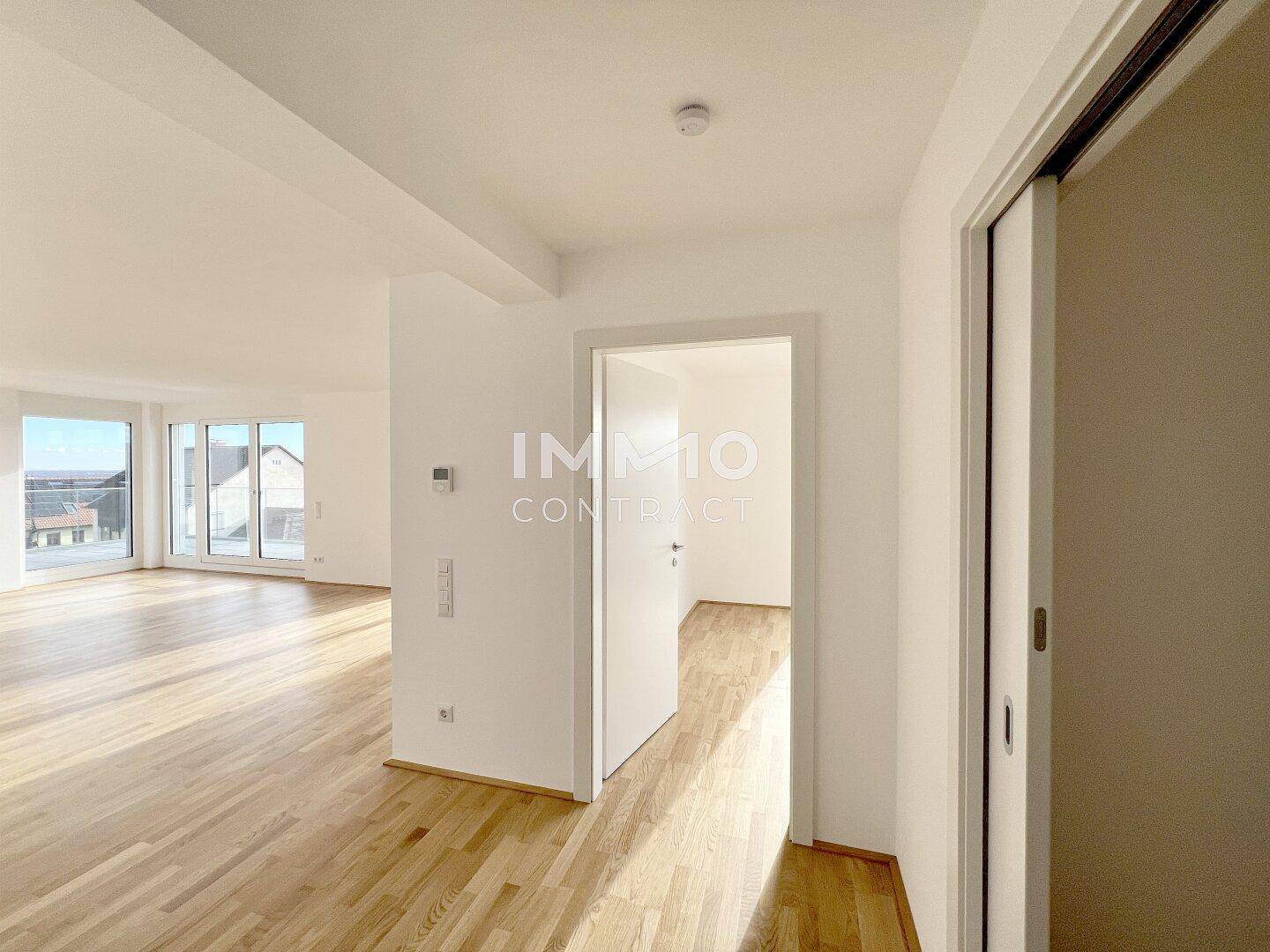 Heller Eingangsbereich mit Holzboden, der in den offenen Wohnbereich mit großen Fenstern führt.