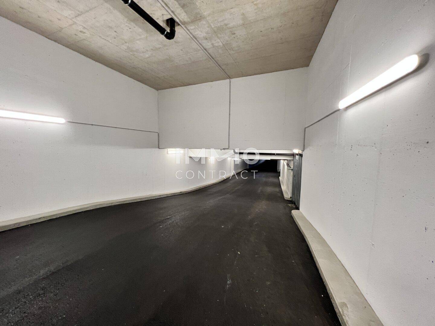 Einfahrt zur Tiefgarage mit Betonwänden und Beleuchtung, führt in den Untergrund.
