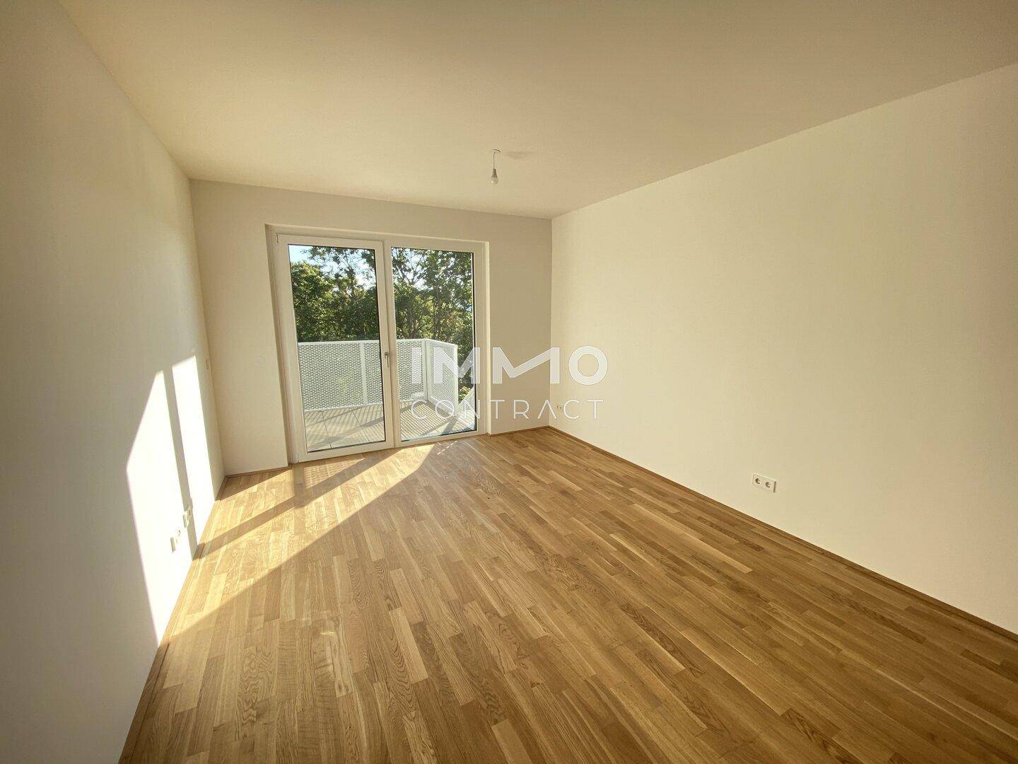Helles Zimmer mit Holzboden und Zugang zu einem Balkon, ideal als Wohn- oder Schlafbereich.