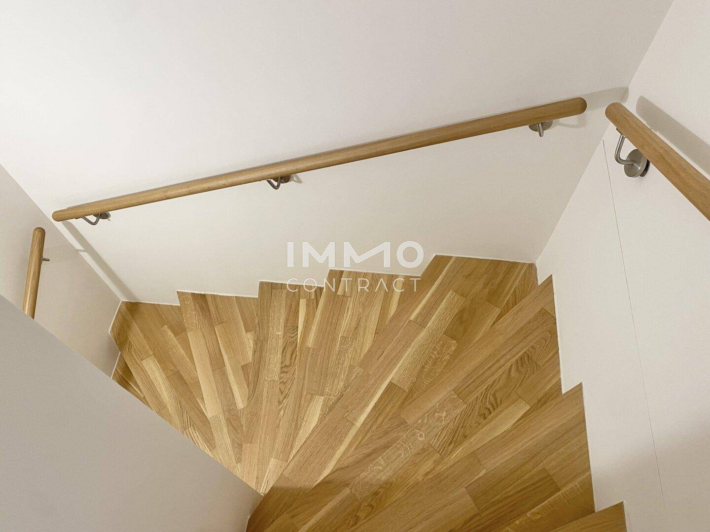 Holztreppe mit hellem Geländer und natürlichem Lichteinfall, verbindet die Etagen.