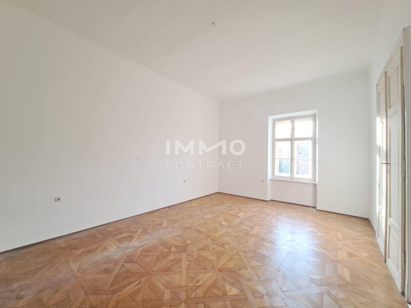 Heller, leerer Raum mit weißen Wänden und einem auffälligen Holzbodenmuster, beleuchtet durch ein Fenster.