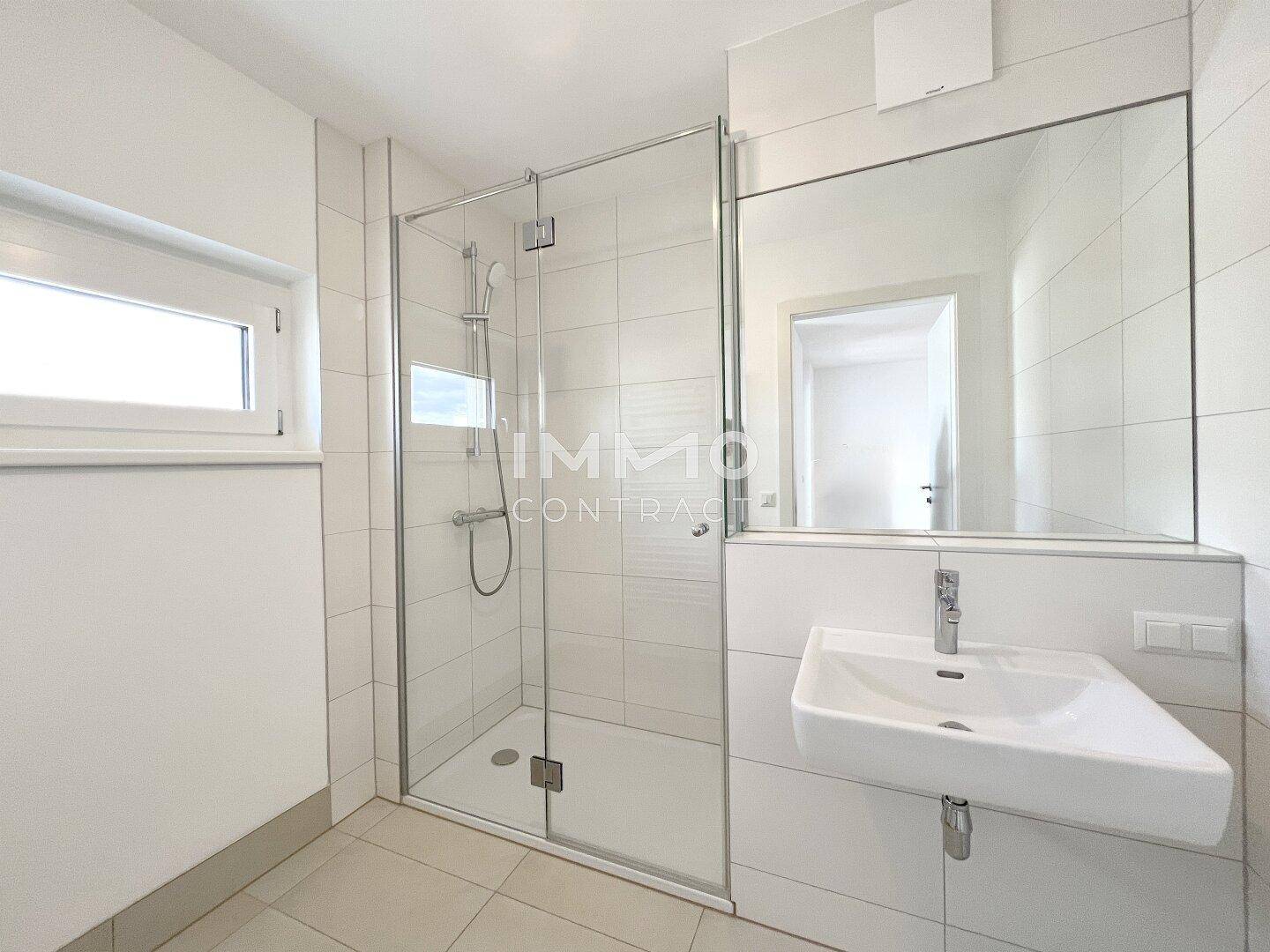 Modernes Badezimmer mit ebenerdiger Dusche, großem Spiegel und Fenster für Tageslicht.