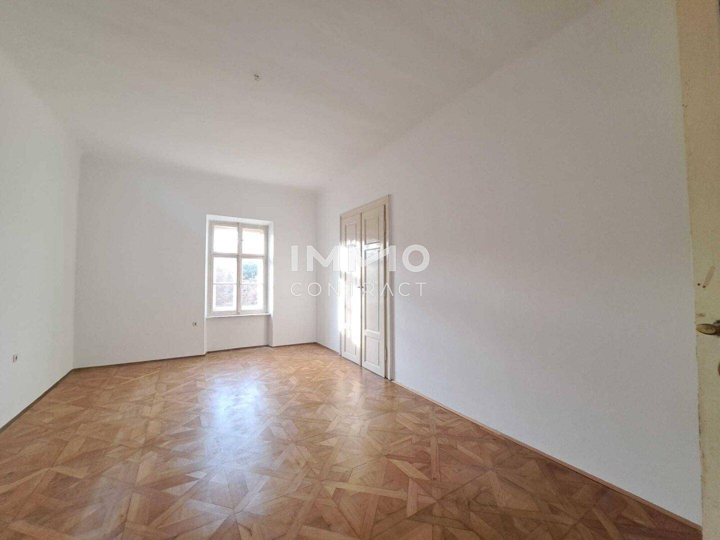 Heller, leerer Raum mit weißen Wänden, einem Fenster und einem Holzboden, der vielseitig nutzbar ist.