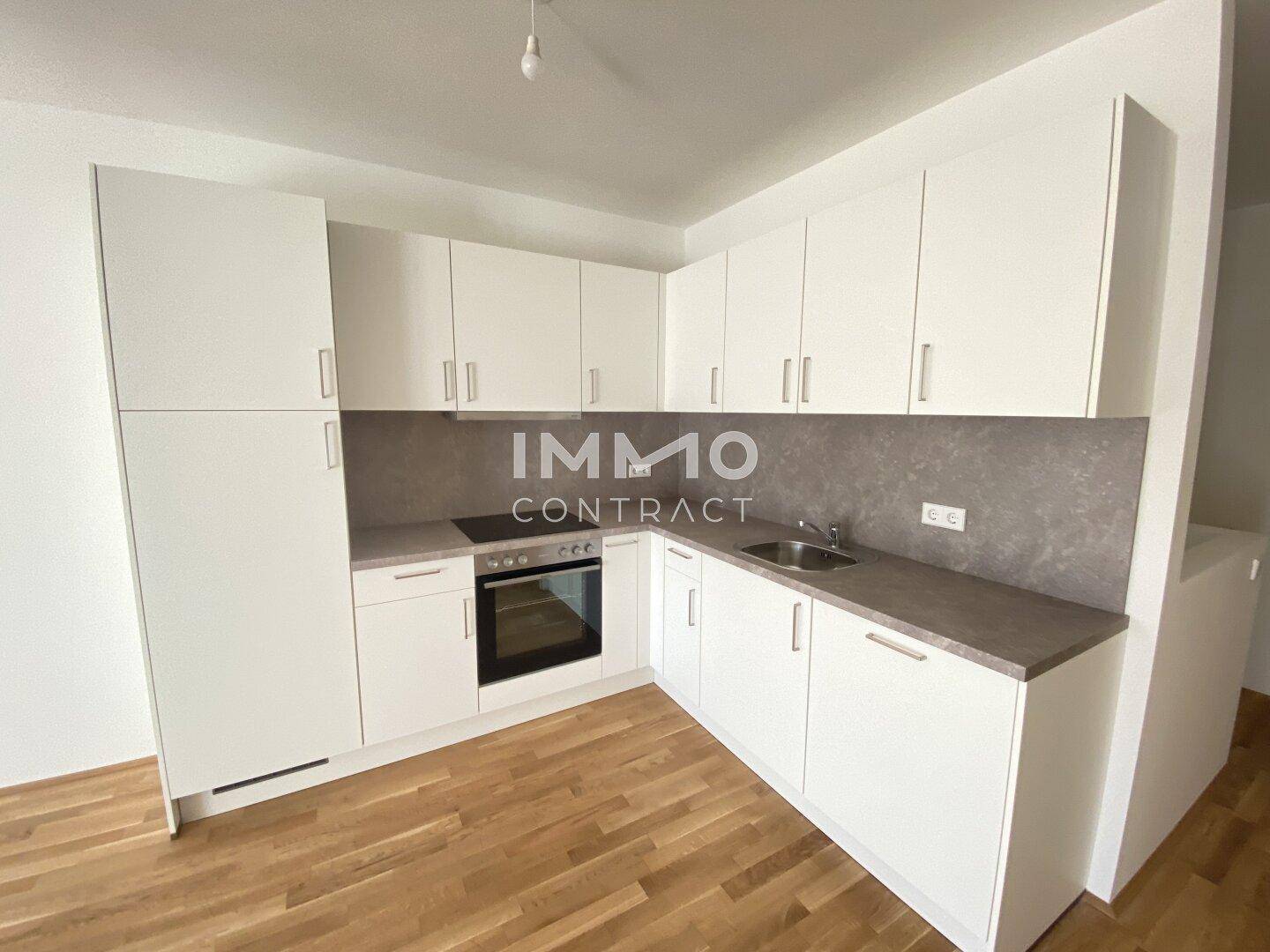 Moderne Einbauküche mit weißen Schränken, integrierten Geräten und Holzboden.