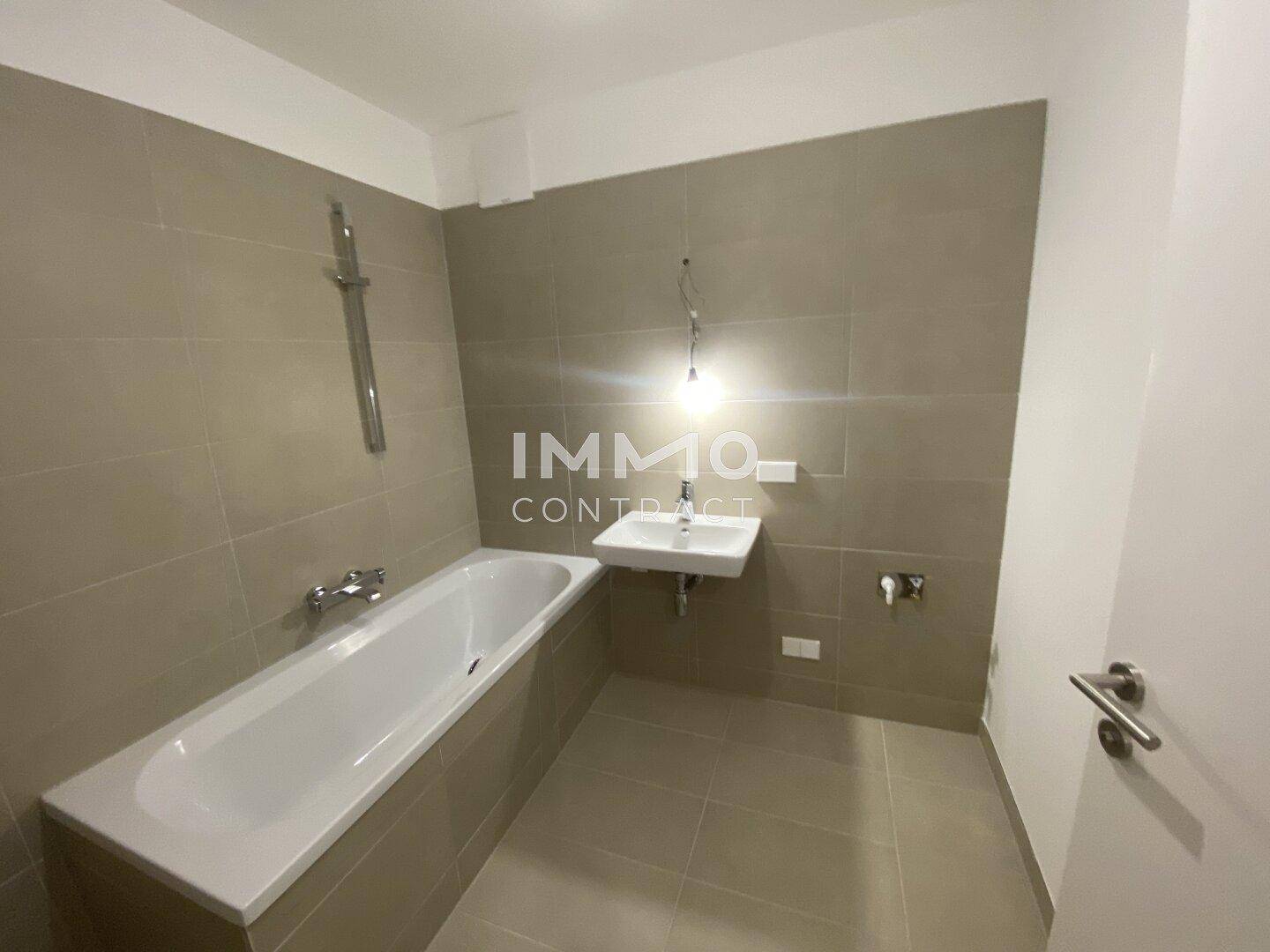Modernes Badezimmer mit Badewanne, Waschbecken und grauen Fliesen.