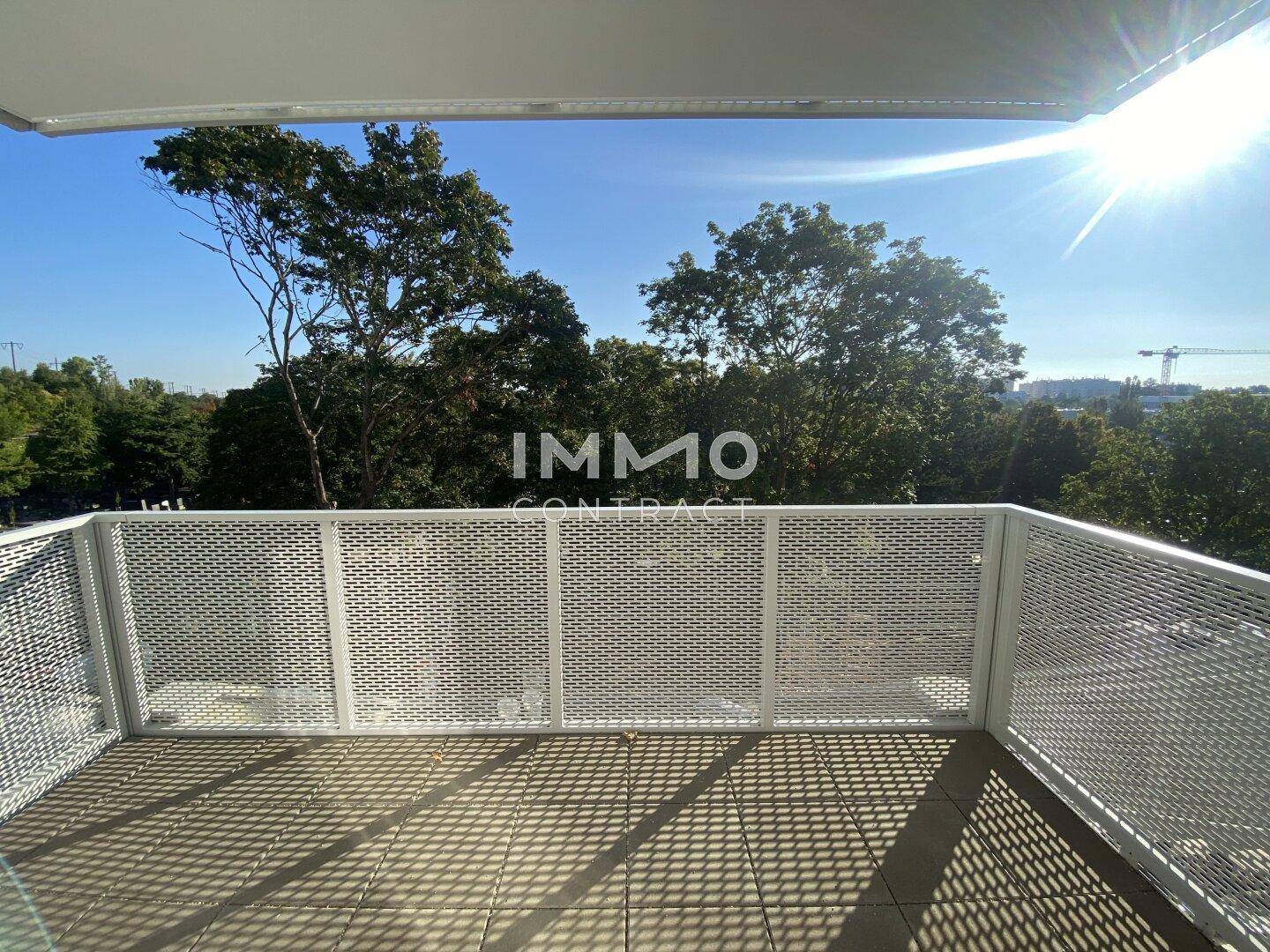Heller Balkon mit moderner Metallbrüstung und sonnigem Ausblick ins Grüne.