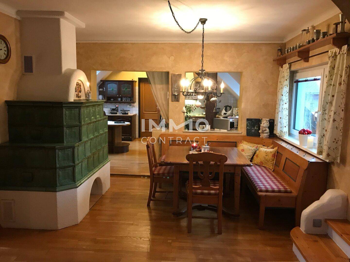 Gemütlicher Essbereich mit Holzboden, Sitzbank und traditionellem grünen Kachelofen.