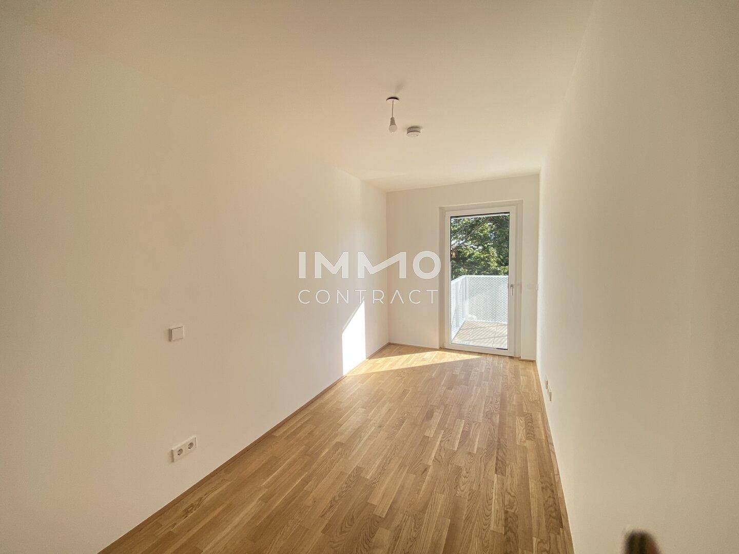 Leerer Raum mit Holzboden und Zugang zu einem Balkon, hell durch Tageslicht.