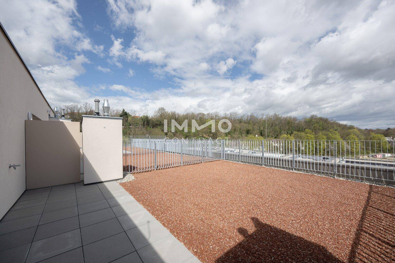Große, unmöblierte Dachterrasse mit Kiesbelag und Blick auf die umliegende grüne Landschaft.