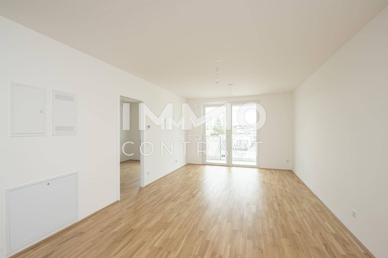Helles Wohnzimmer mit Parkettboden und Zugang zu einem Balkon, ideal für natürliche Belichtung.