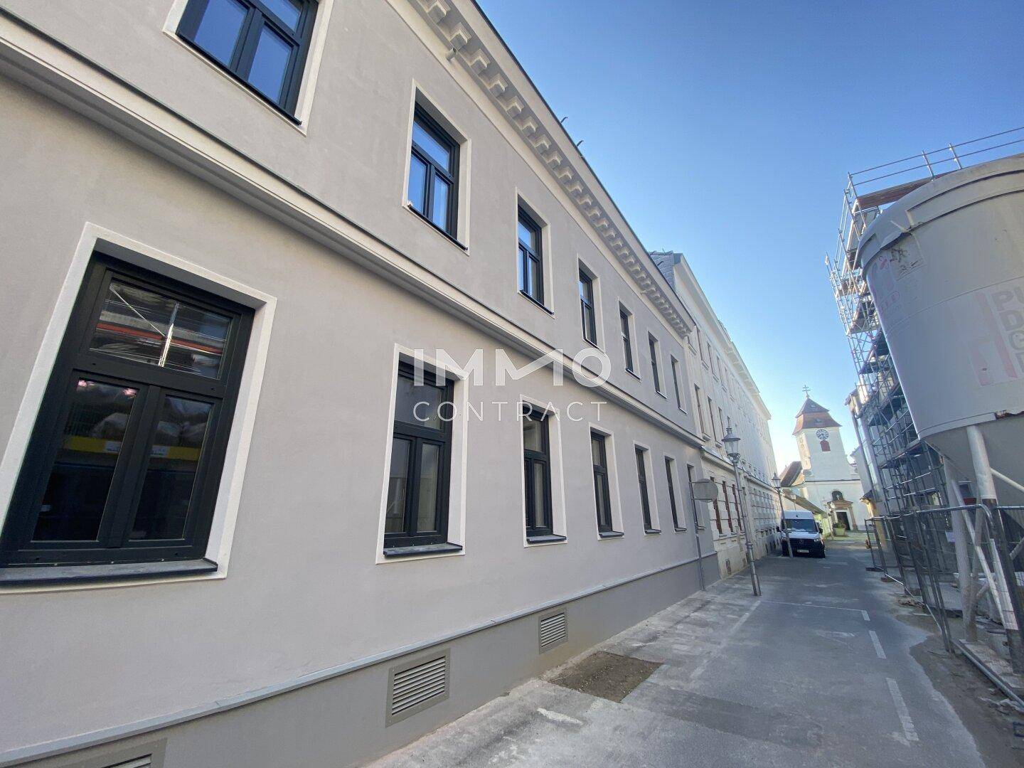 Historisches Gebäude mit grauer Fassade und schwarzen Fenstern an einer ruhigen Straße.