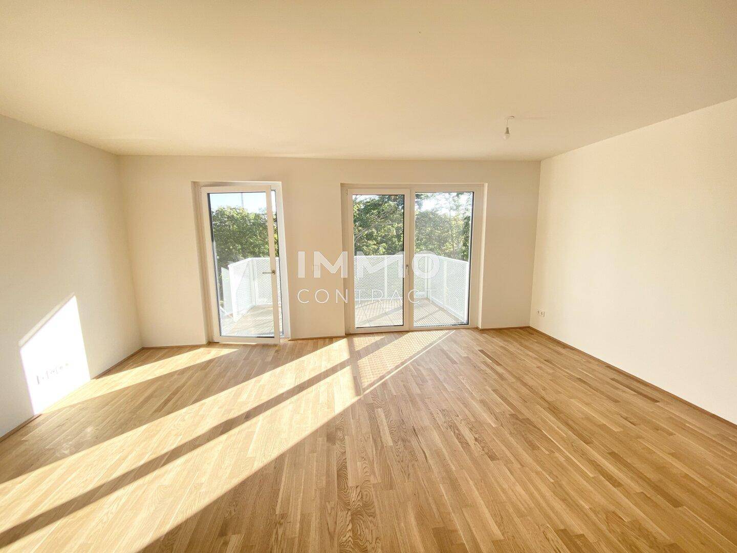 Geräumiger, unmöblierter Raum mit hellem Holzboden und großen Fenstern, die viel Tageslicht hereinlassen.