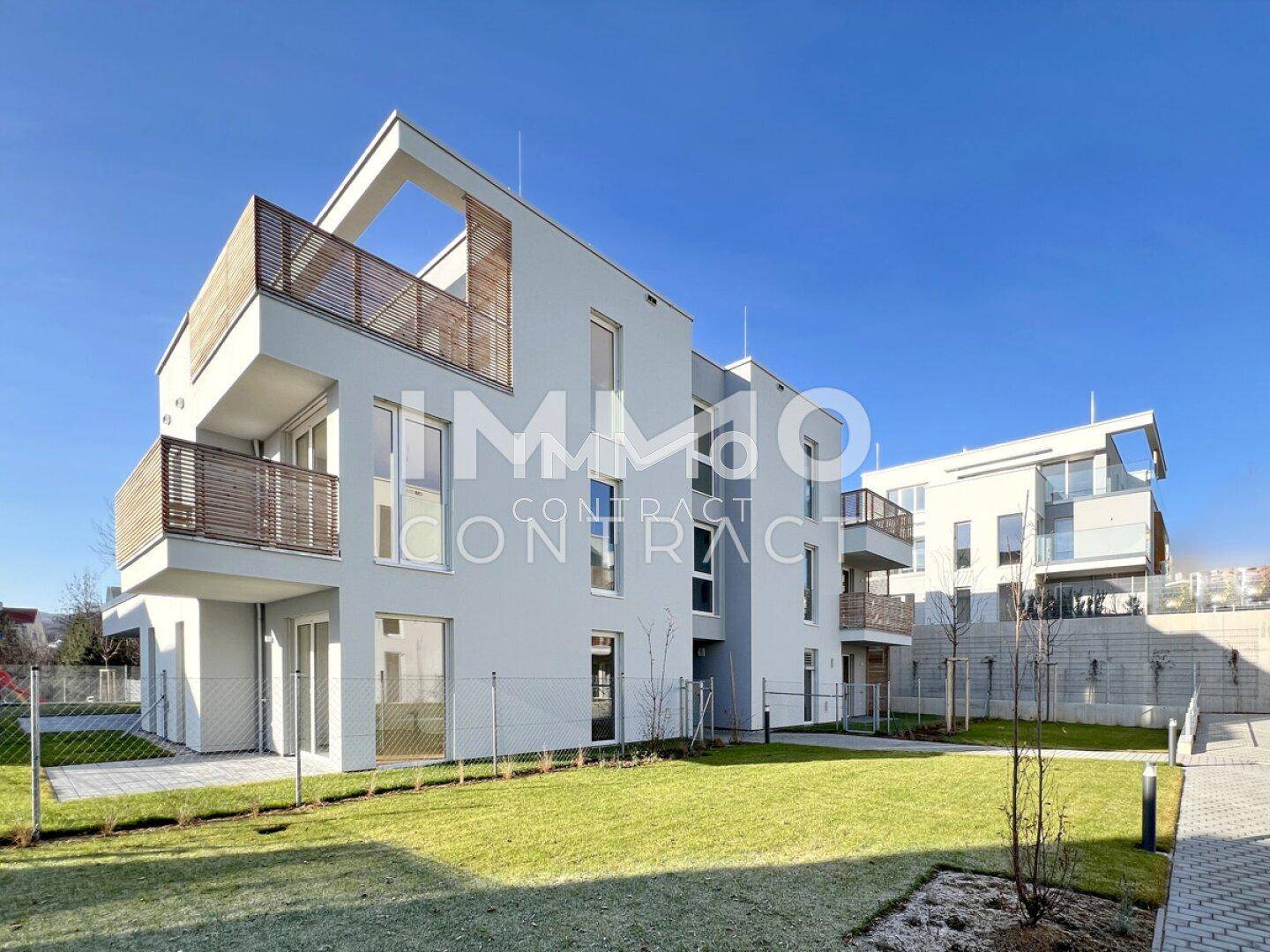 Neubauwohnanlage mit moderner Architektur, gepflegtem Rasen und sonnigem Außenbereich.