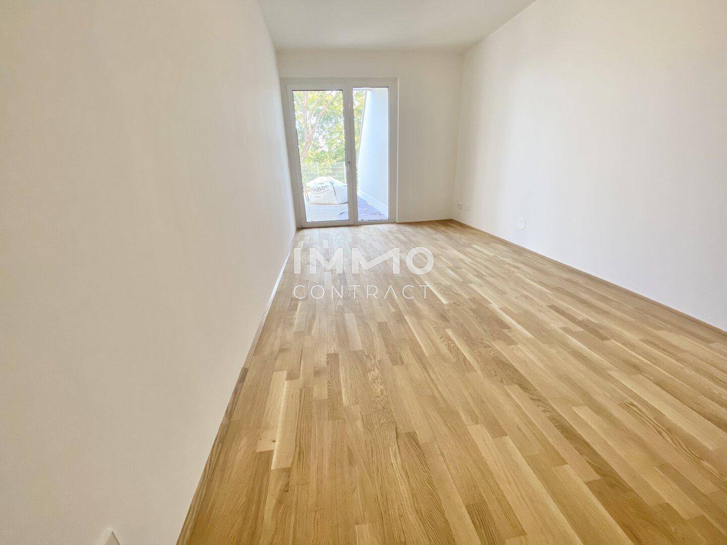 Geräumiger, unmöblierter Raum mit hellem Holzboden und Zugang zu einem Balkon.