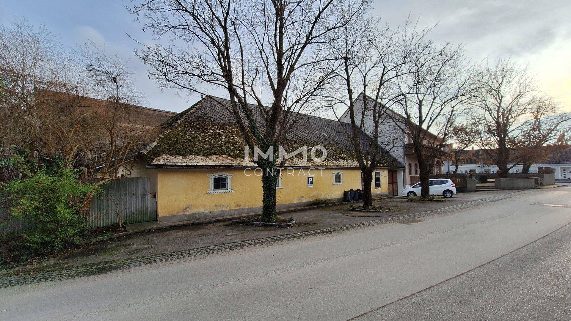 Gelbes Nebengebäude mit altem Dach und Parkplatz an der Straße.