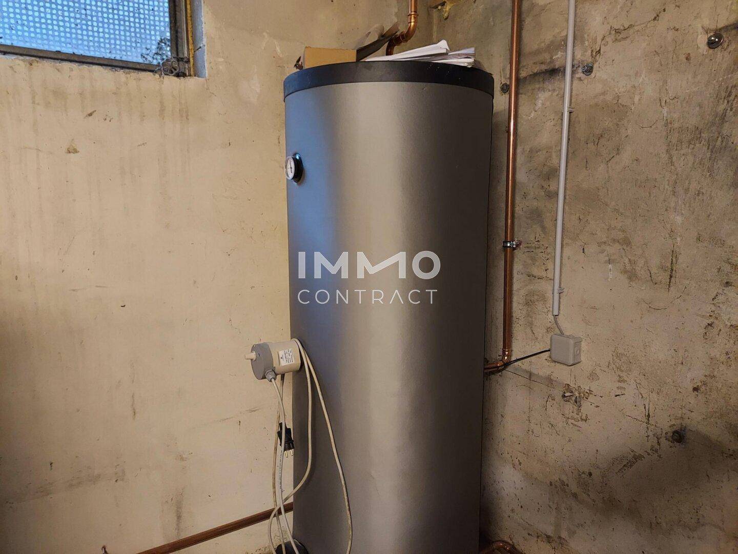 Heizungsraum mit großem Warmwasserspeicher und blanken Wänden.